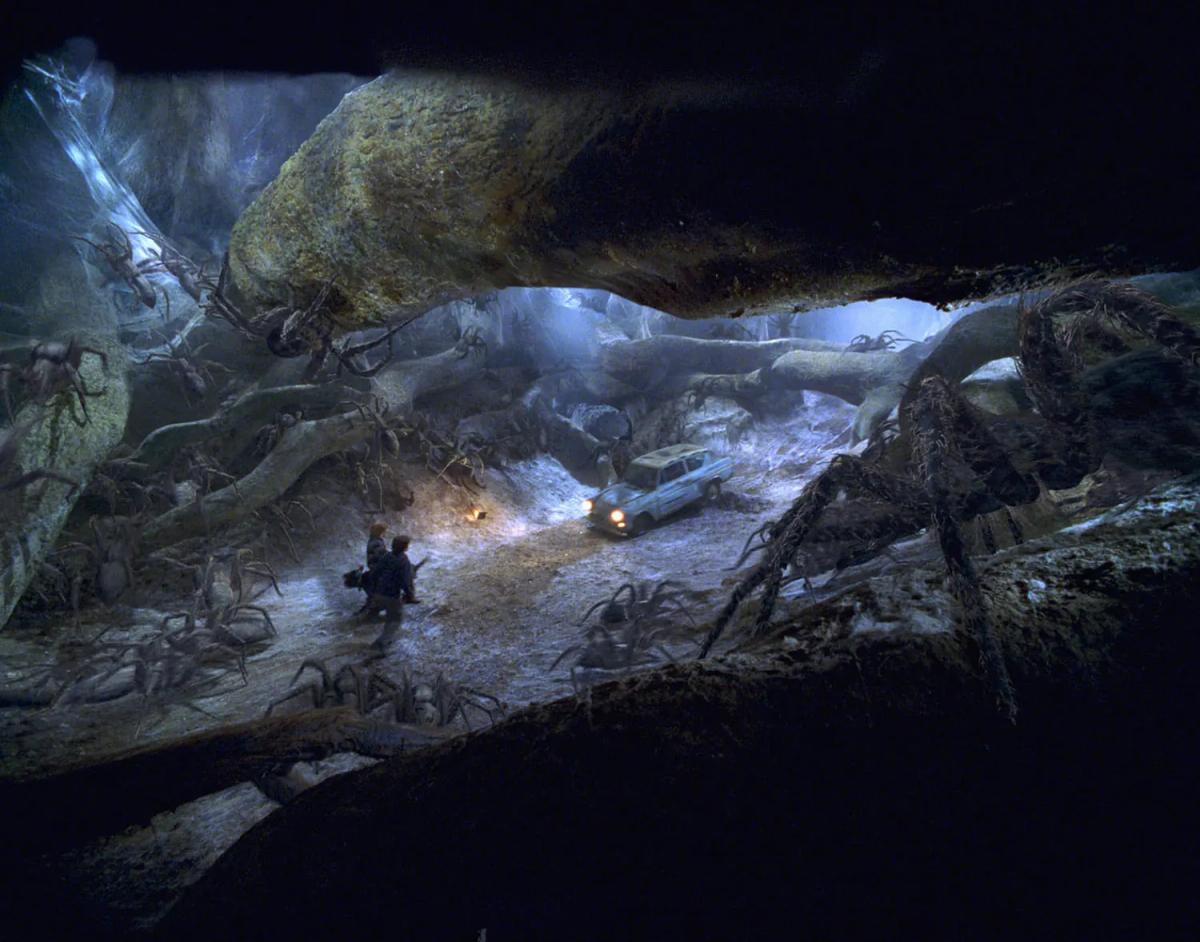 Harry Potter (Daniel Radcliffe) and Ron Weasley (Rupert Grint) stand back to back in a hollow in the Forbidden Forest as giant spiders close in around them, the Ford Anglia behind.