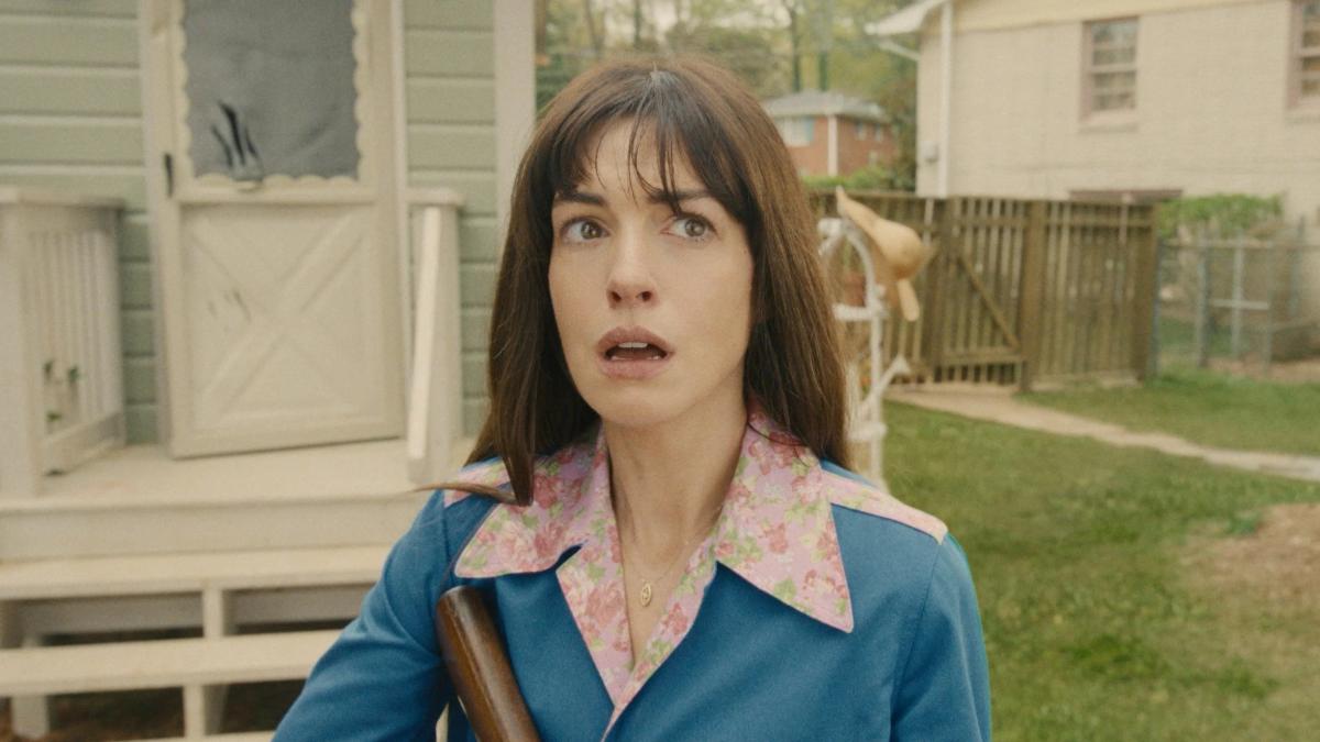 Denise Platt standing in a suburban back garden holding a wooden club, looking upward with her mouth open in alarm.