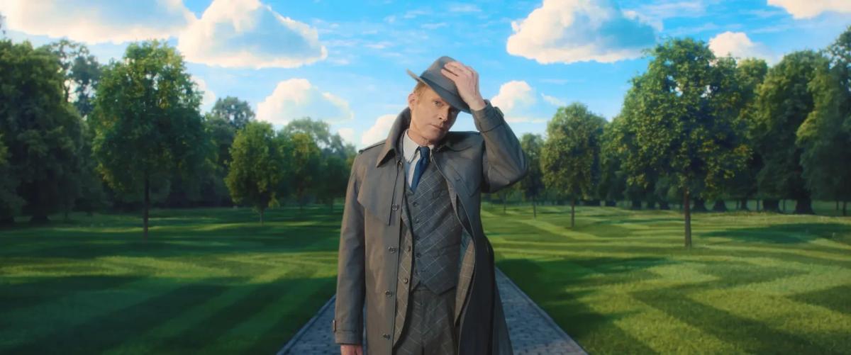 Paul Bettany as Vision in a grey trench coat tips his hat on a tree-lined path under a bright blue sky in VisionQuest