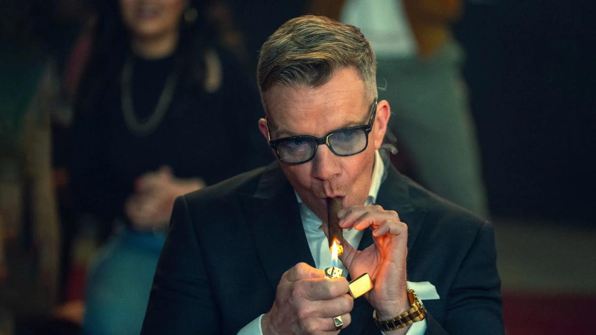 Max Beesley as boxing promoter Henry Collins, lighting a cigar with a gold lighter.