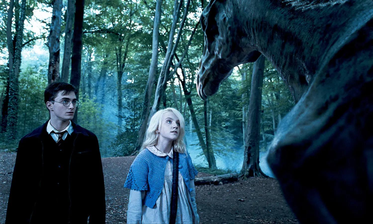 Daniel Radcliffe as Harry Potter and Evanna Lynch as Luna Lovegood stand beside a Thestral in the forest.