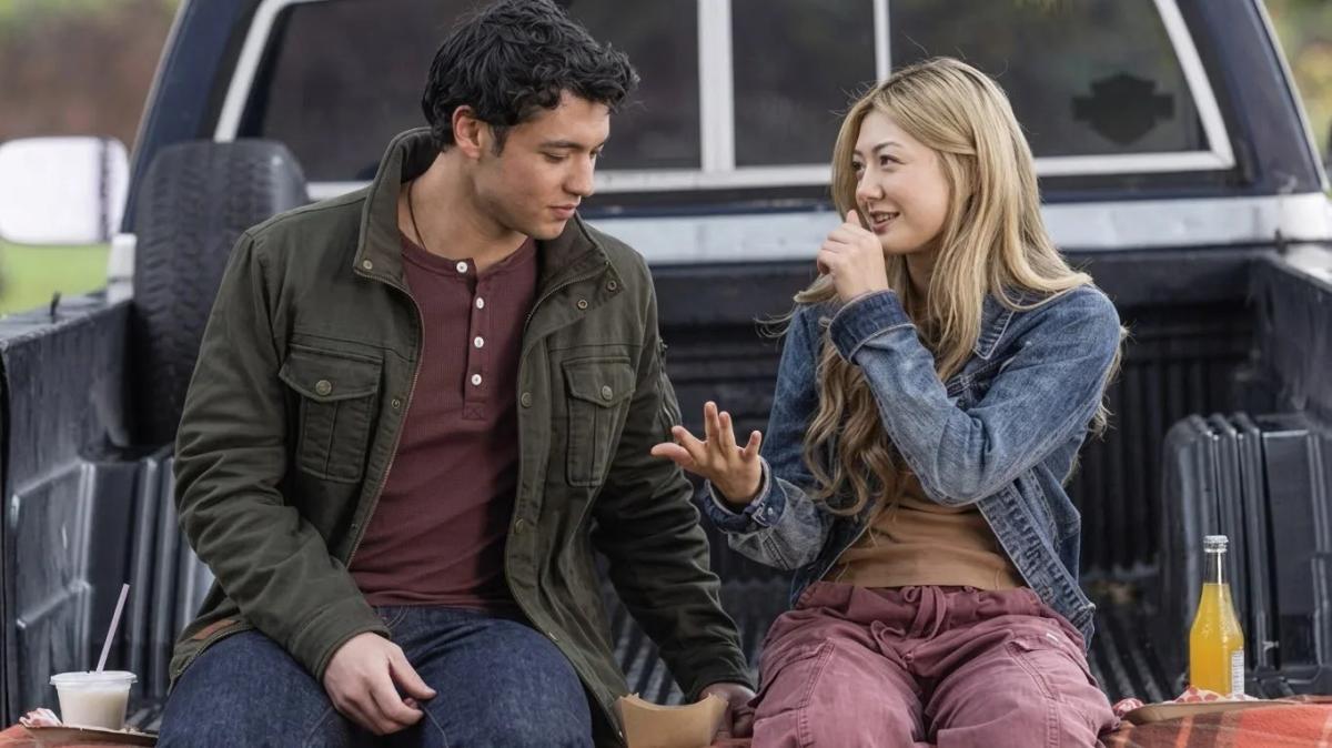 Cam Dillinger (Kyle Clark) and Teagan Tao (Miku Martineau) sitting and talking in the back of his pickup truck.