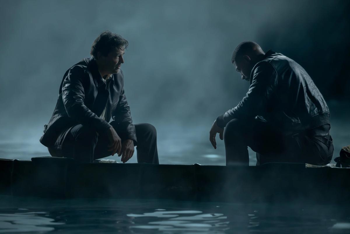 Kyle Chandler as the Halogram and Aaron Pierre as John Stewart sitting at either end of a small boat on dark, misty water.