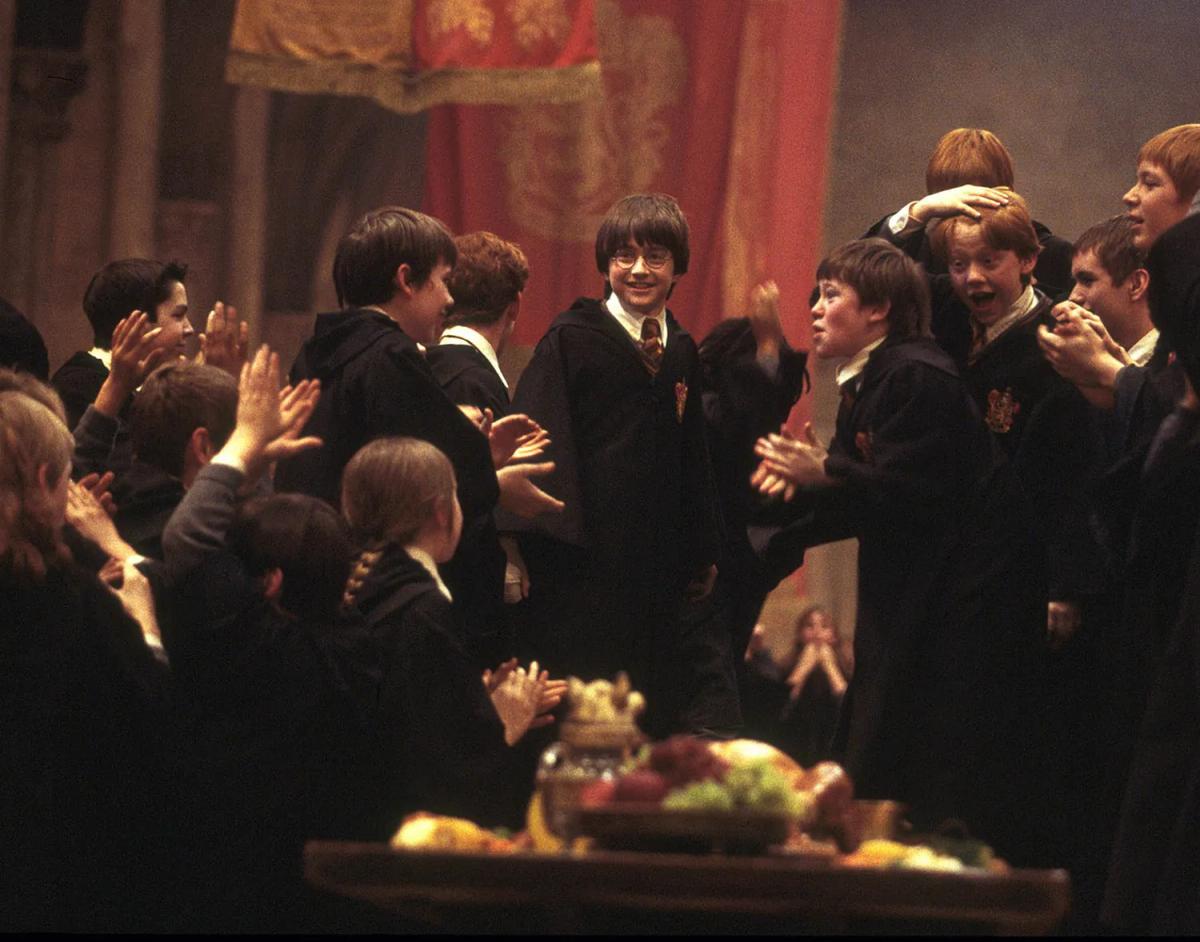 Daniel Radcliffe as Harry Potter and Rupert Grint as Ron Weasley celebrate with Gryffindor students in the Great Hall.