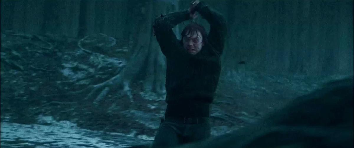 Ron Weasley (Rupert Grint) raises the Sword of Gryffindor over his head beside a frozen forest pool, about to bring it down on the locket.