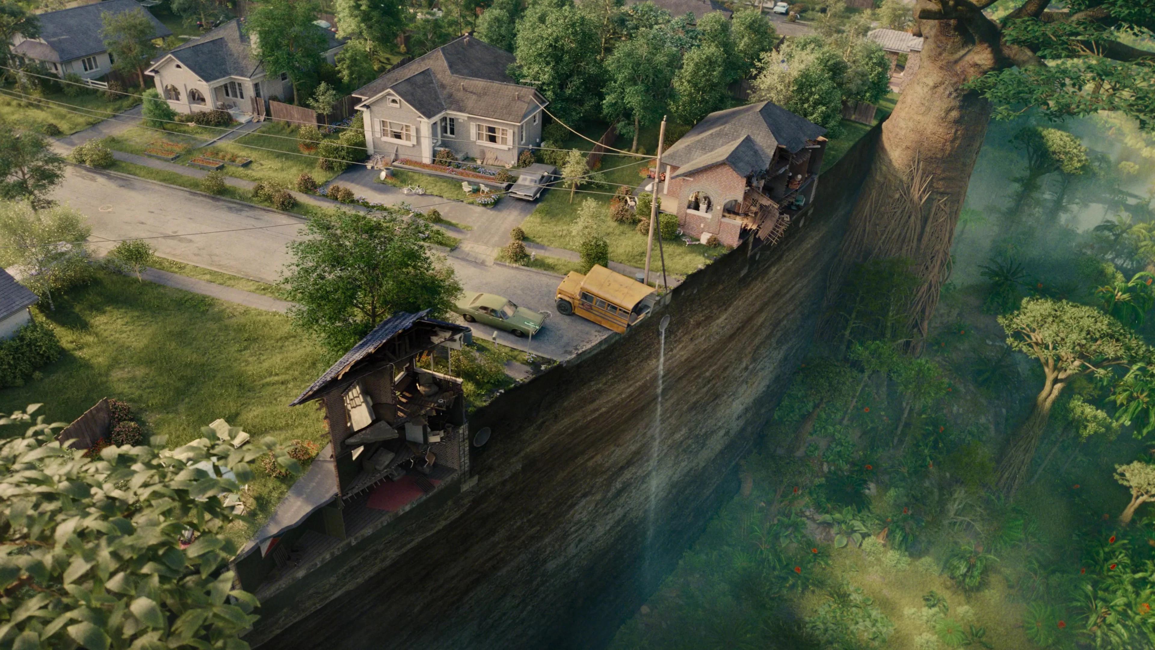 Aerial view of a suburban street sheared off mid-block, houses and a school bus at the lip of a sheer drop into prehistoric forest.