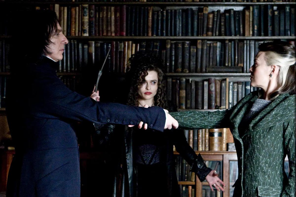 Alan Rickman as Severus Snape and Helen McCrory as Narcissa Malfoy clasp hands while Helena Bonham Carter as Bellatrix Lestrange holds her wand beside them.