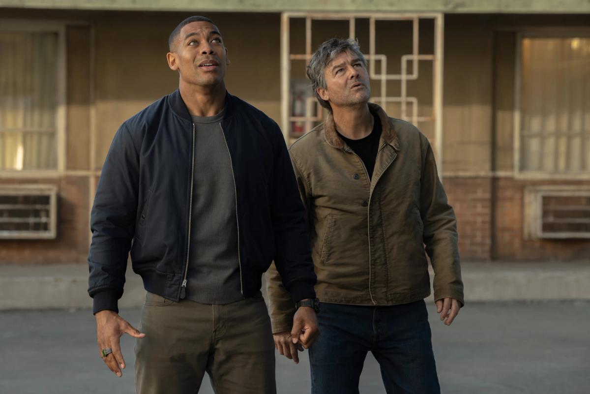 Aaron Pierre as John Stewart and Kyle Chandler as Hal Jordan standing outside a motel, both looking up at the sky.