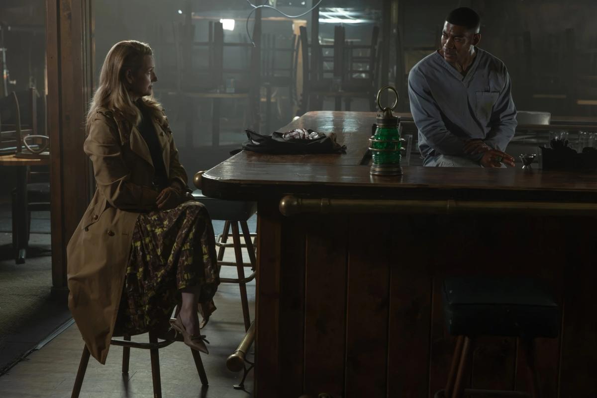 Laura Linney as Lianna sitting at a bar opposite Aaron Pierre as John Stewart, with a green lantern and a crystallised heart on the counter between them.