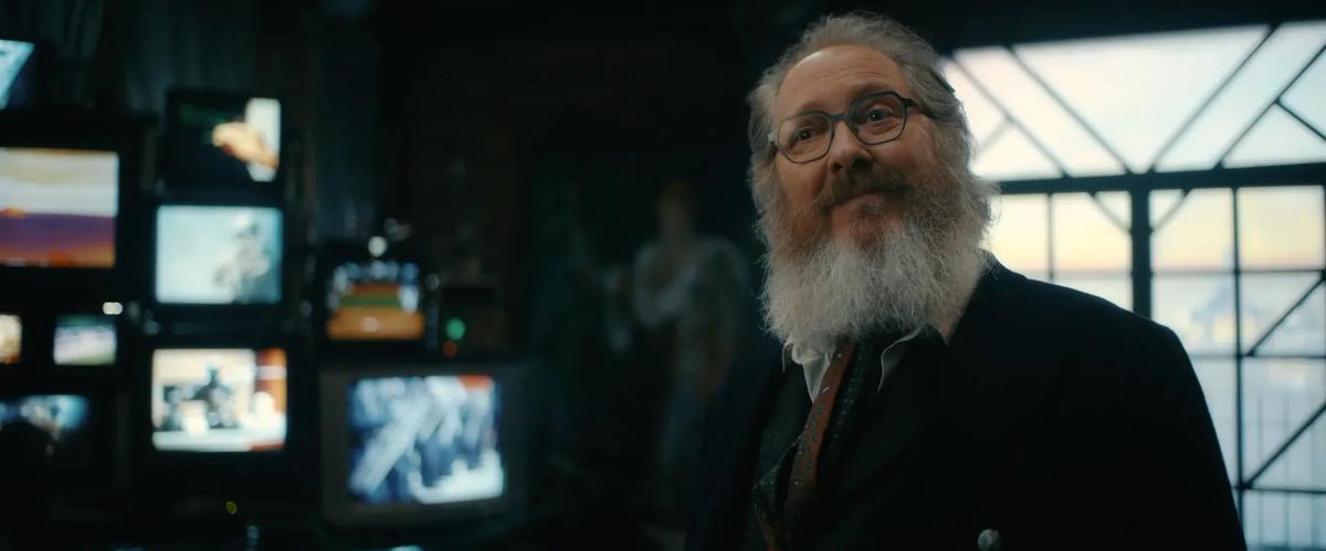 James Spader as Ultron in human form, bearded and wearing glasses, in a room full of old television monitors in VisionQuest
