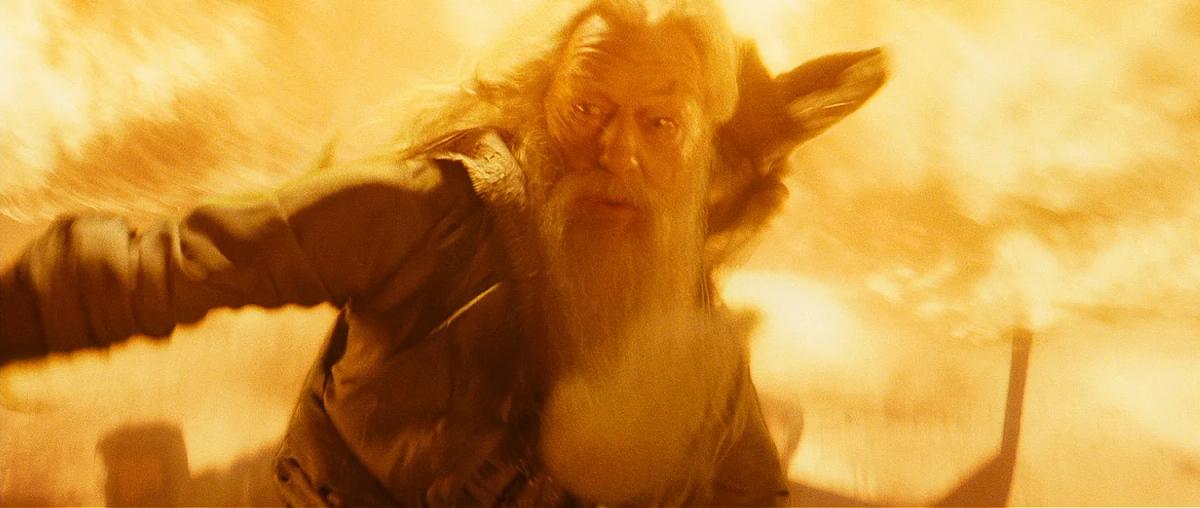 Michael Gambon as Albus Dumbledore raises his wand amid fire in the cave.