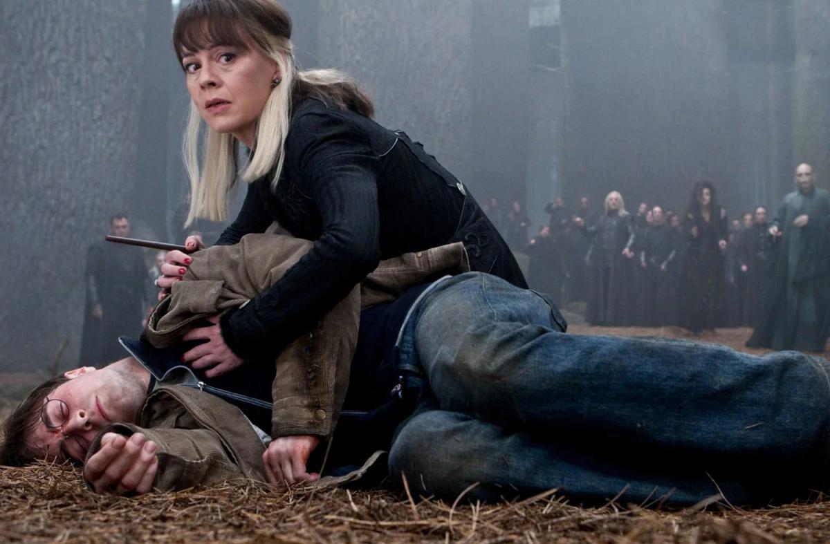 Helen McCrory as Narcissa Malfoy crouching over Daniel Radcliffe as Harry Potter on the forest floor, her hand on his chest.