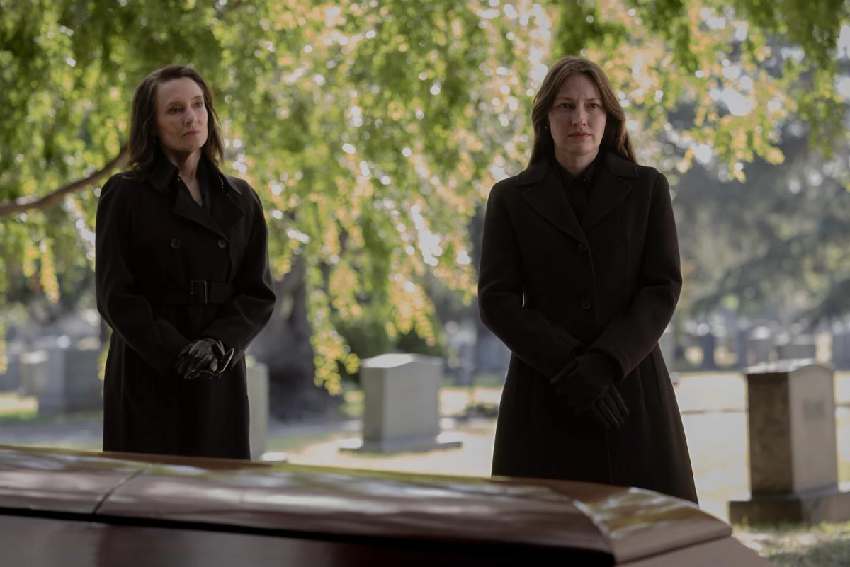 Amie MacKenzie as Carol Ferris and Kelly Macdonald as Kerry Kane standing at a graveside beside a coffin.