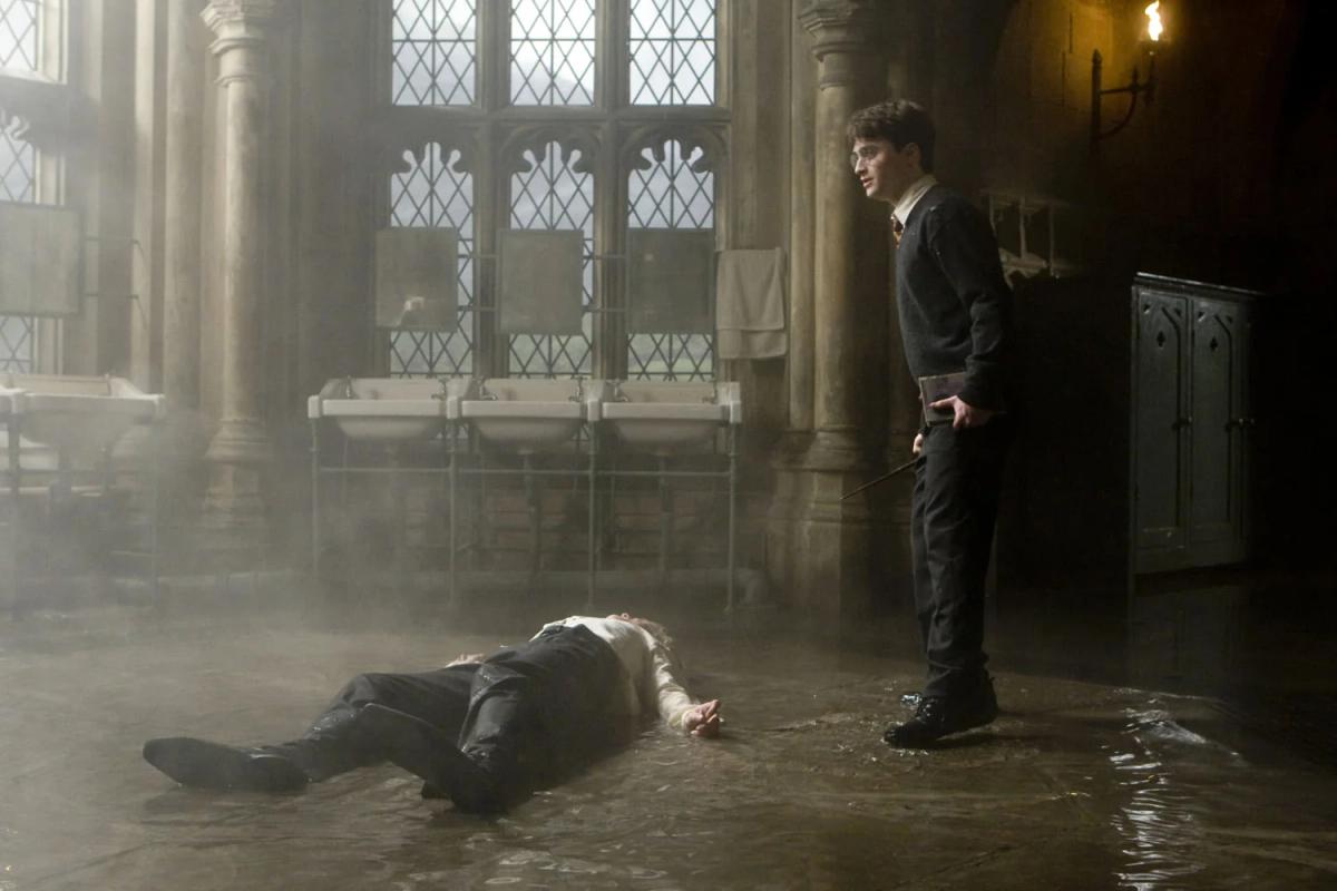 Daniel Radcliffe as Harry Potter stands over Tom Felton as Draco Malfoy on the flooded bathroom floor.