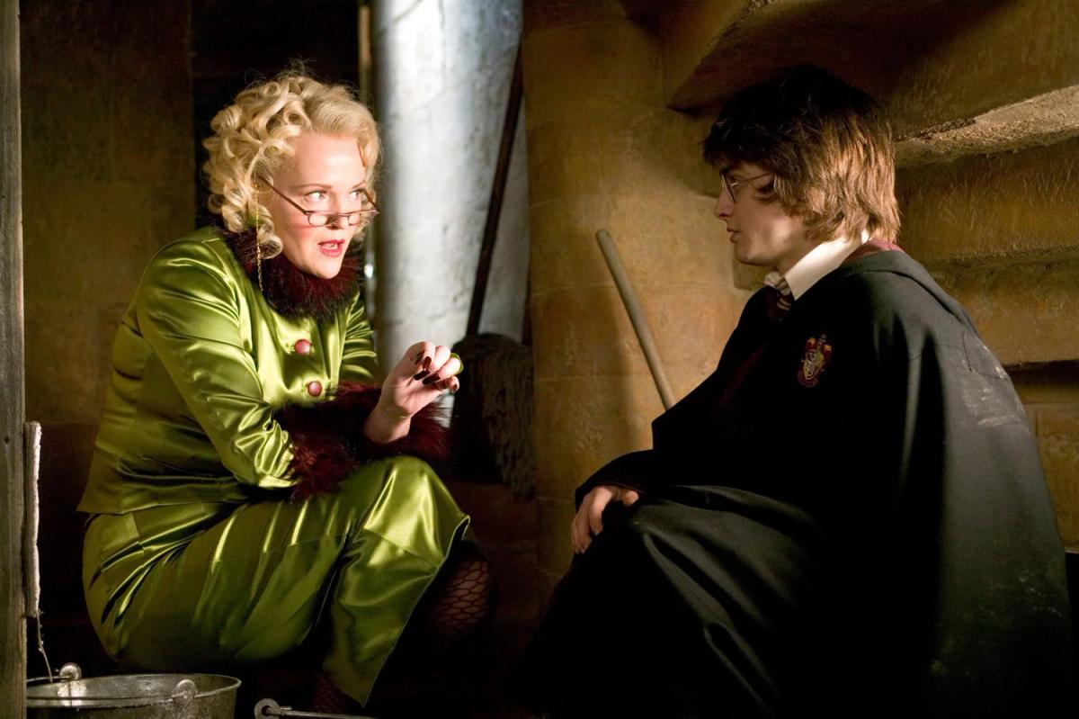 Miranda Richardson as Rita Skeeter, dressed in green, leans towards Daniel Radcliffe as Harry Potter in a cramped broom cupboard.