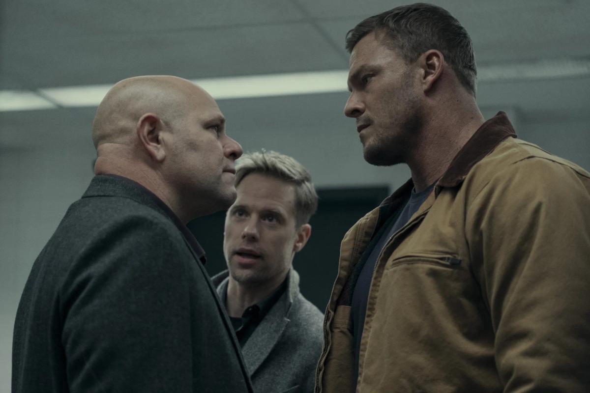 Domenick Lombardozzi as Guy Russo squares up face to face with Alan Ritchson as Jack Reacher, with Shaun Sipos as David O'Donnell caught between the two of them.