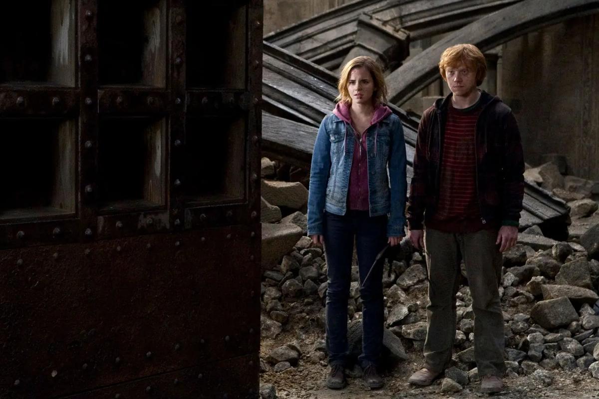 Emma Watson as Hermione Granger and Rupert Grint as Ron Weasley standing together in a corridor of broken stone during the Battle of Hogwarts.