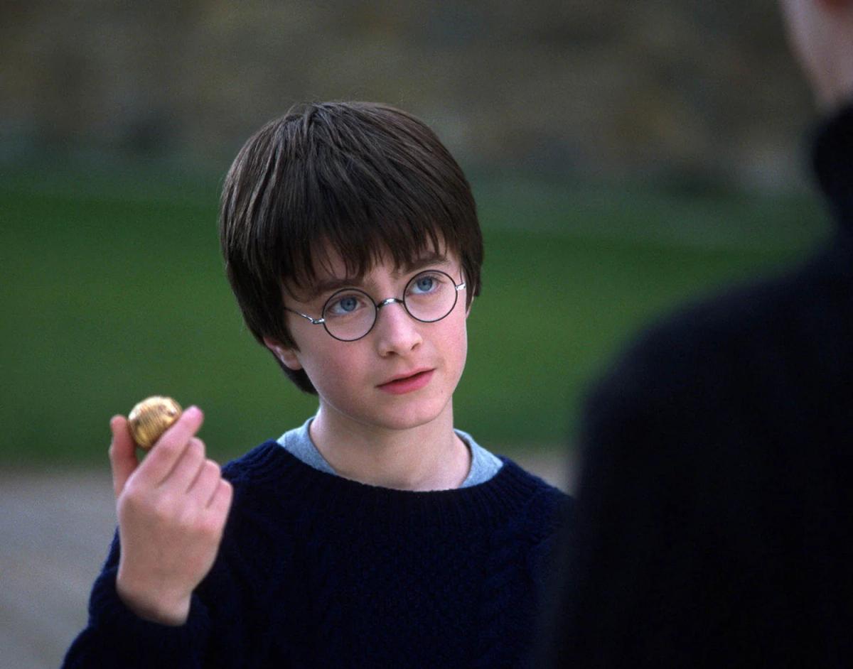 Harry Potter (Daniel Radcliffe) holding the Golden Snitch between his fingers on the Hogwarts grounds.