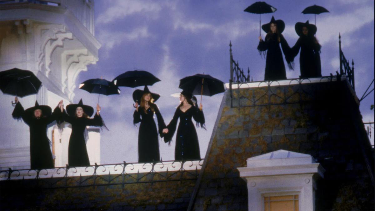 Women in black hats and dresses standing along the roof of the Owens house holding open black umbrellas.