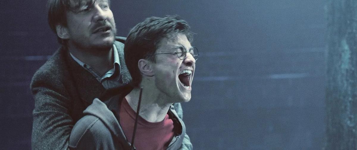 Remus Lupin (David Thewlis) grips a screaming Harry Potter (Daniel Radcliffe) from behind to hold him back.