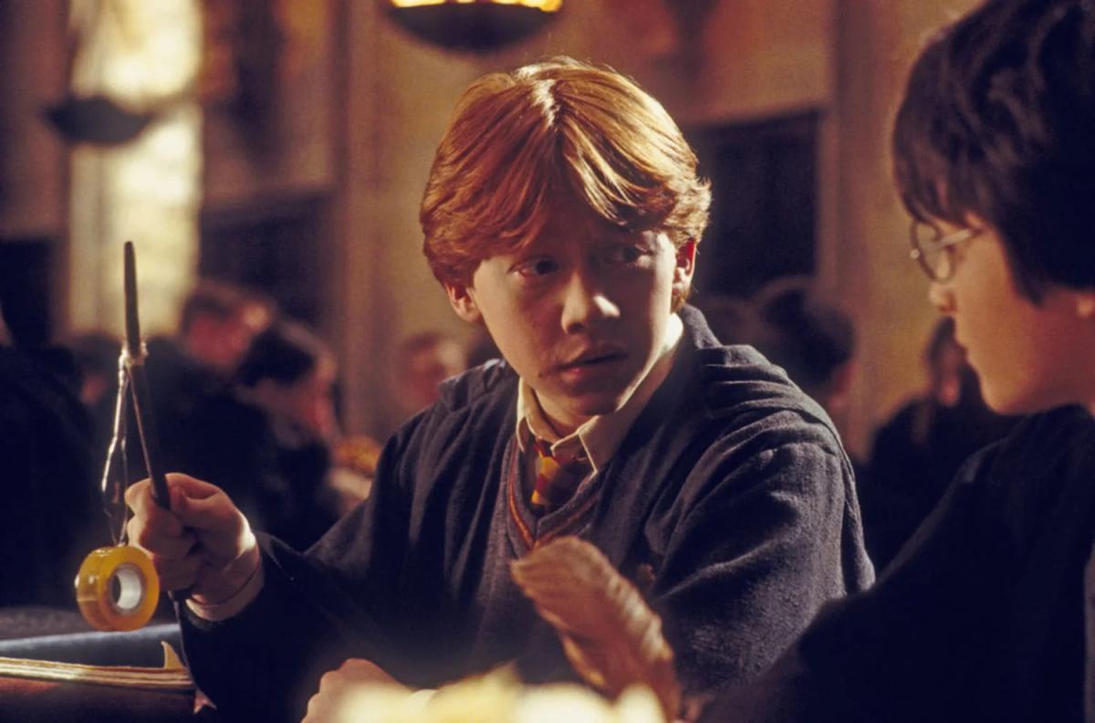 Rupert Grint as Ron Weasley shows his broken wand to Daniel Radcliffe as Harry Potter at a table.