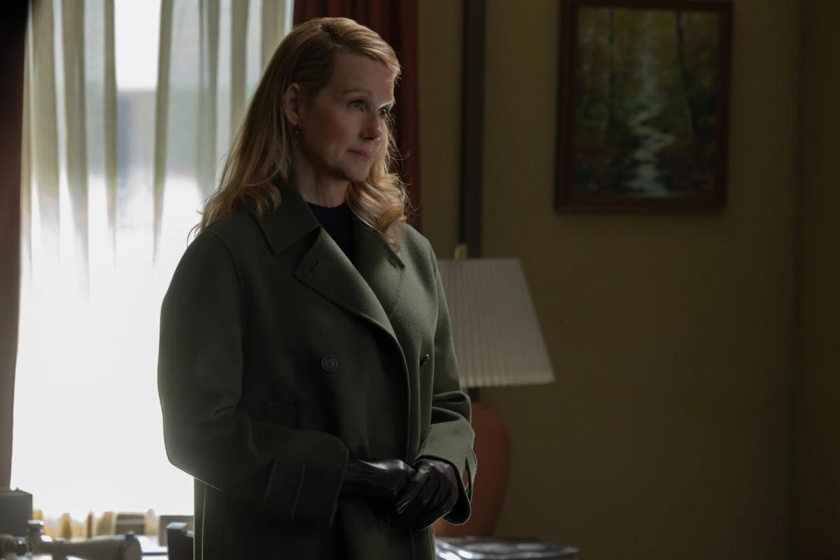 Laura Linney as Lianna, a Guardian of the Universe in human form, standing in a motel room in a green coat and leather gloves.
