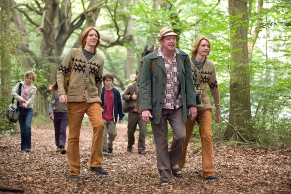 Mark Williams as Arthur Weasley walks through the woods with Fred and George Weasley, played by James and Oliver Phelps, with Hermione and Harry following behind.