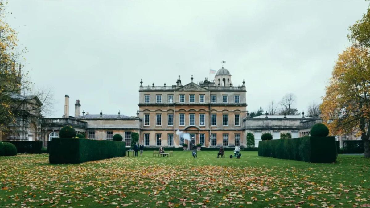 The front of Halstead Manor seen across the lawn on an overcast autumn day, with fallen leaves and clipped hedges in the foreground.