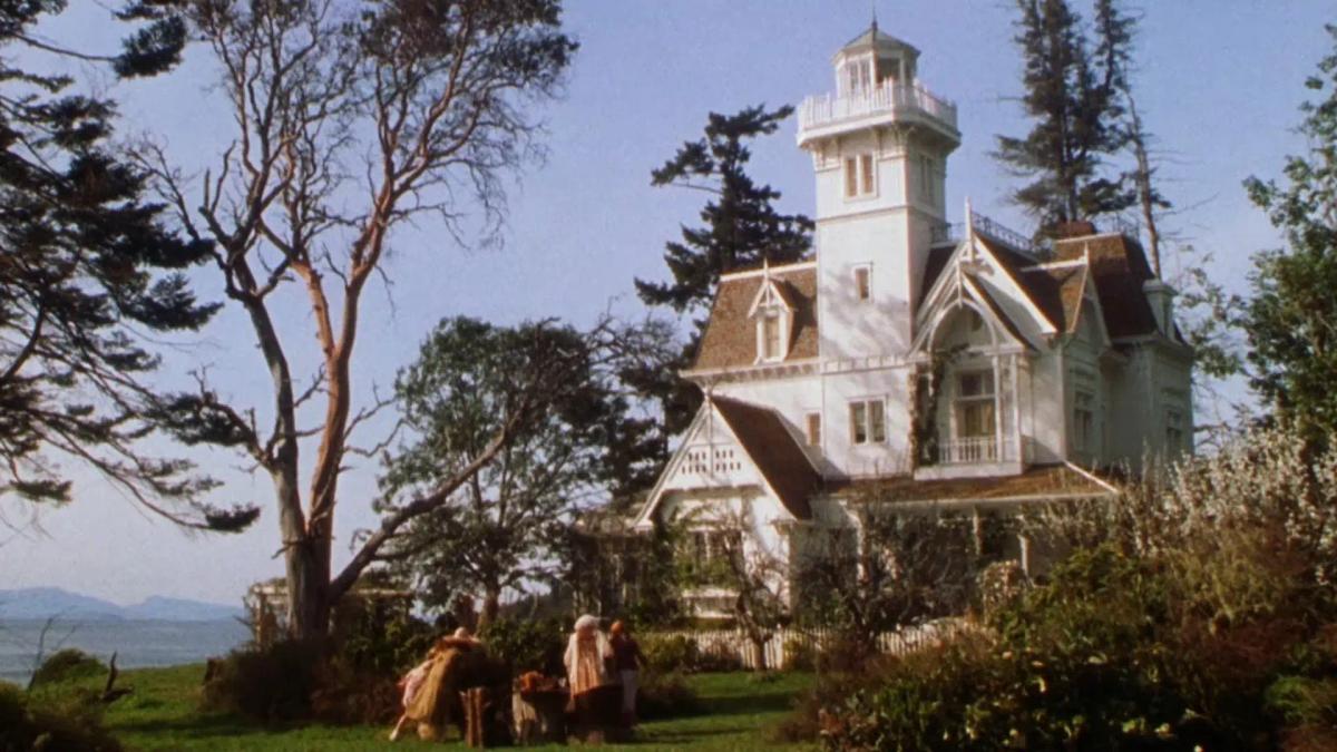 The white Victorian Owens house from Practical Magic, seen across its garden with the water behind it.