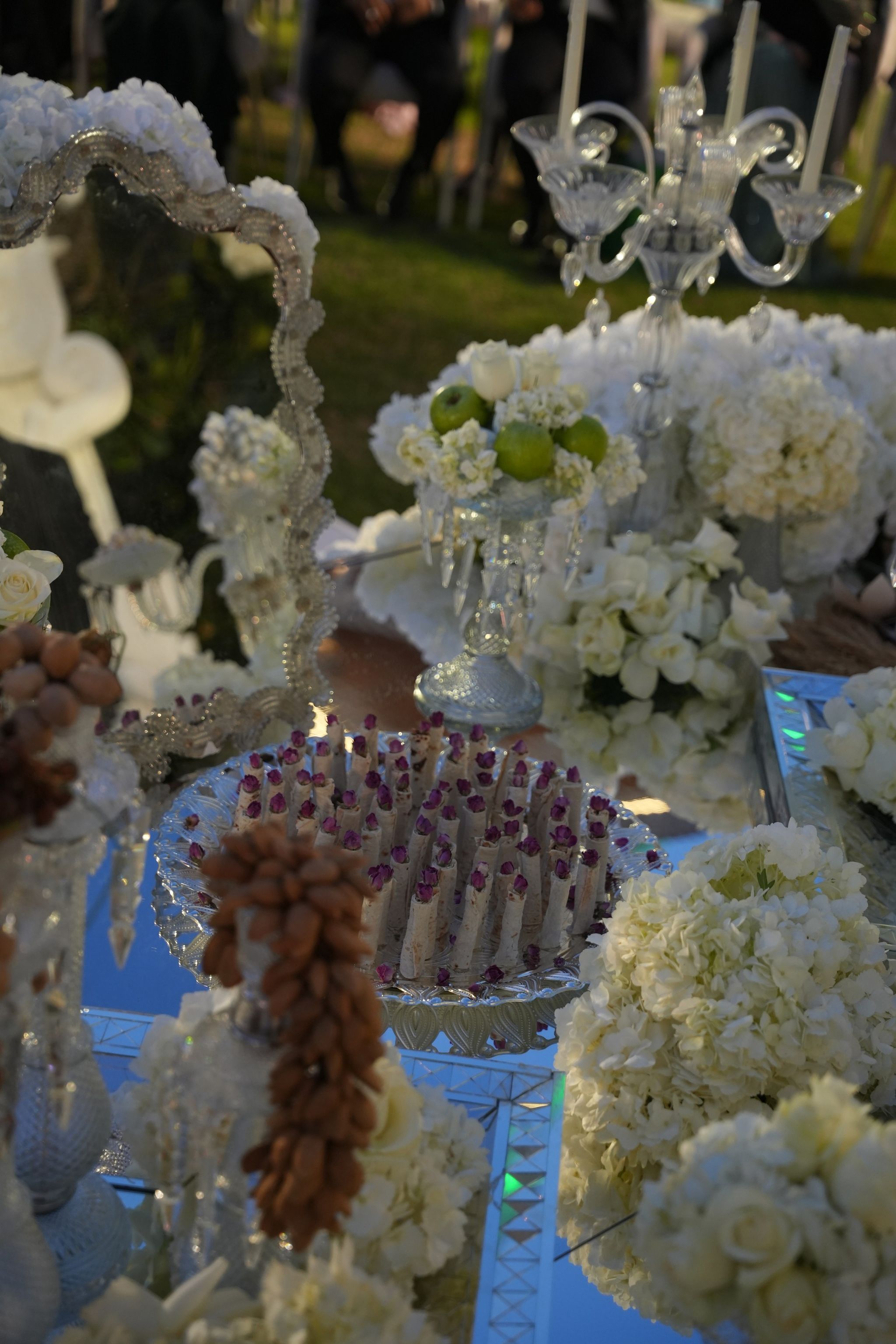 Ornate mirror, crystal candelabra and a tray of rosebud-topped sweets on the sofreh at dusk