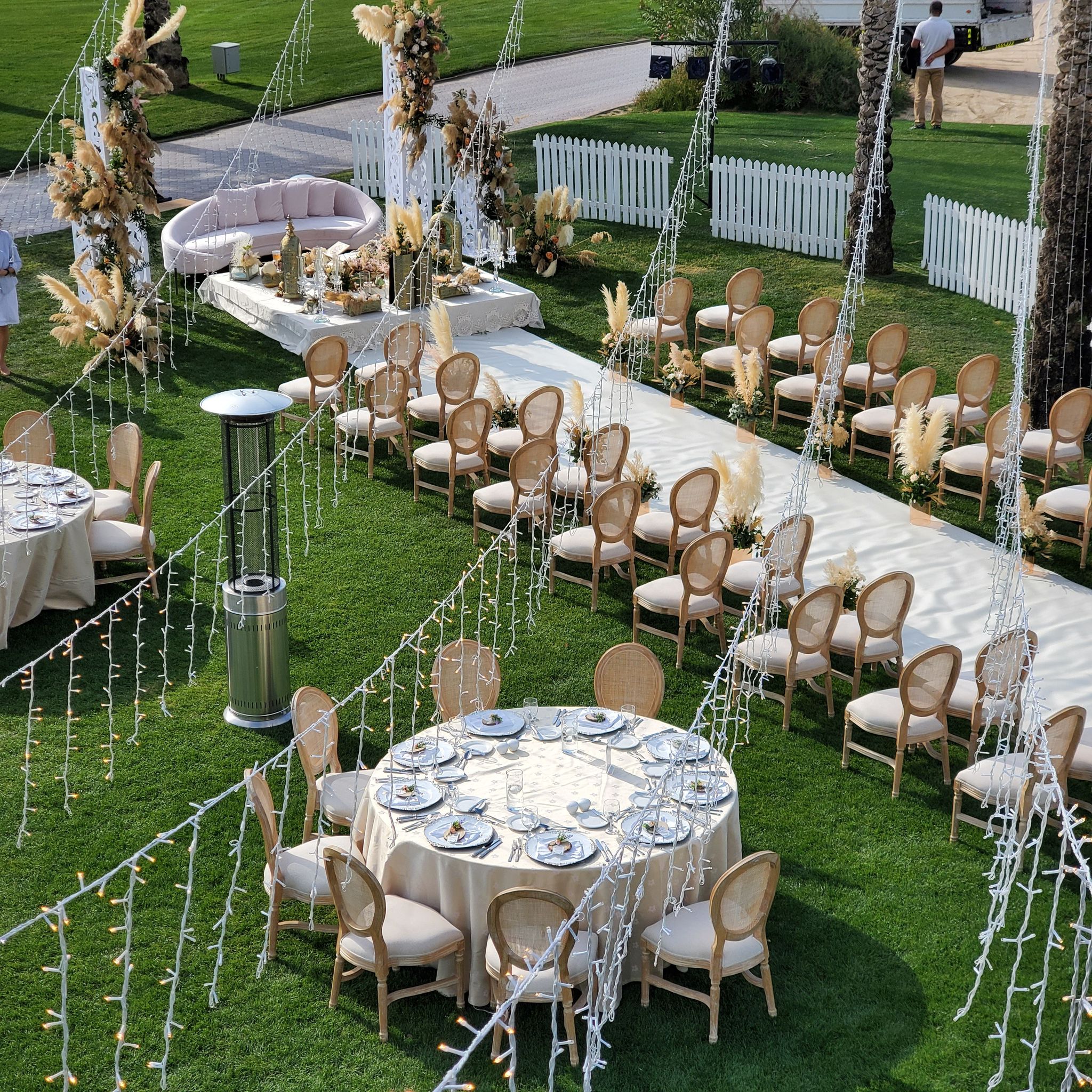 Elevated view of the lawn ceremony aisle, dining tables and fairy-light curtains strung between palms