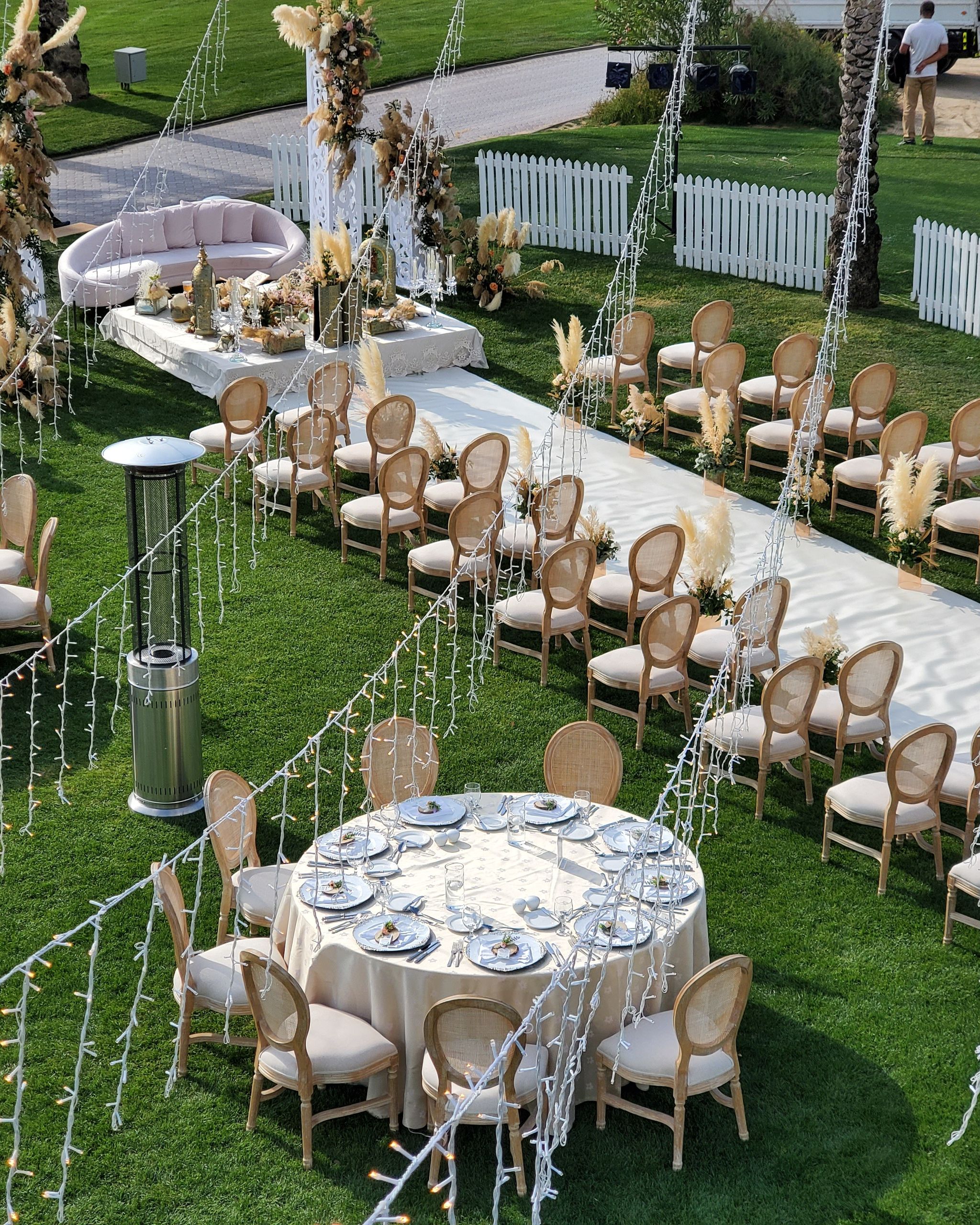 Elevated view of the lawn ceremony aisle, dining tables and fairy-light curtains strung between palms