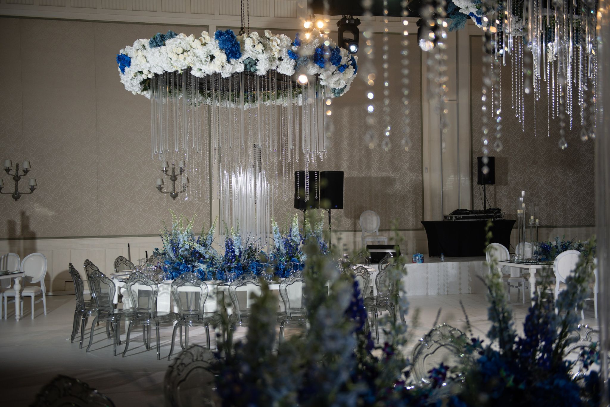 Floating ring of white and blue hydrangeas above a round table of delphiniums and clear chairs