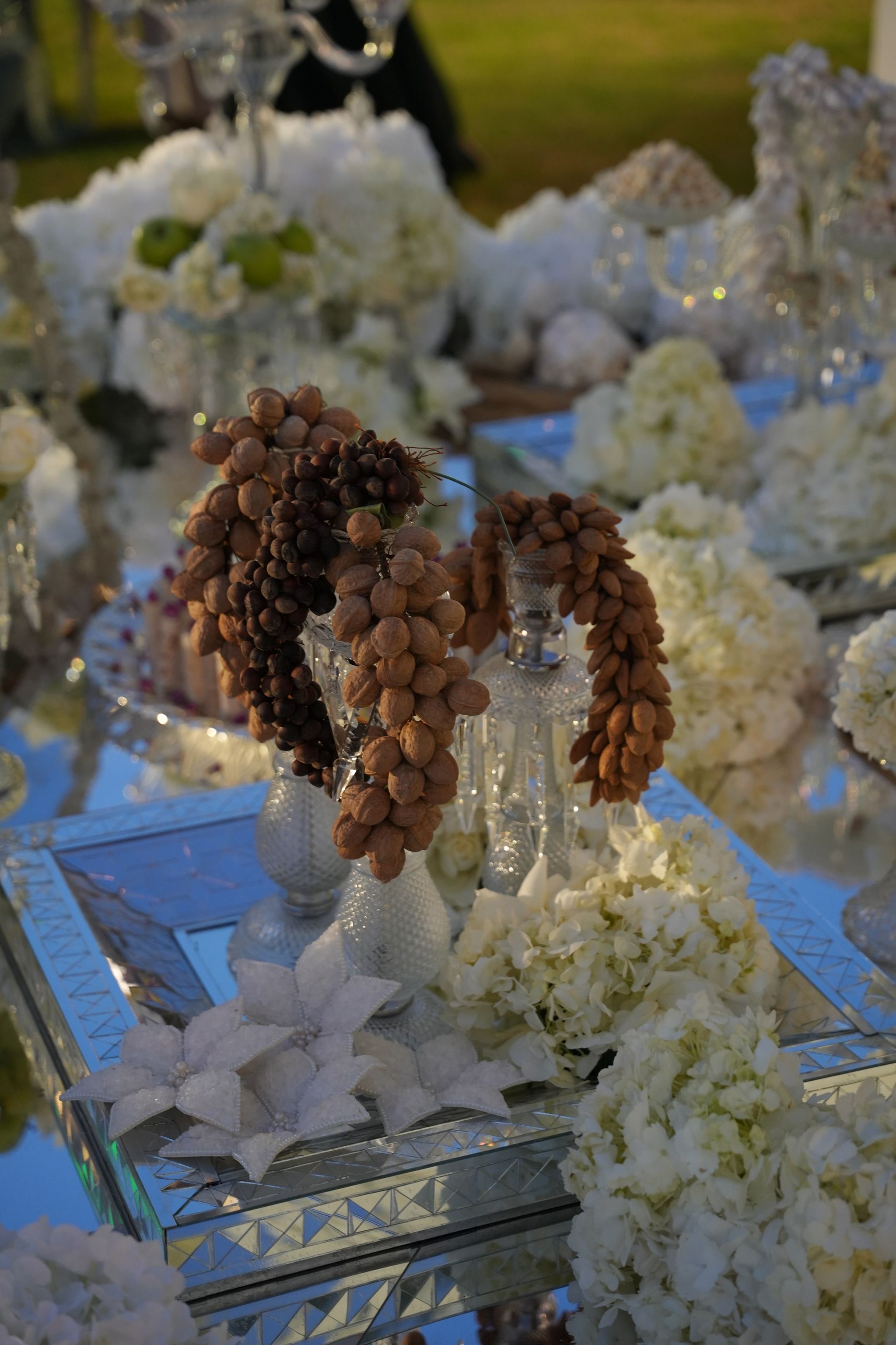 Garlands of almonds and dried grapes on cut-crystal stands among white hydrangeas on a mirrored table