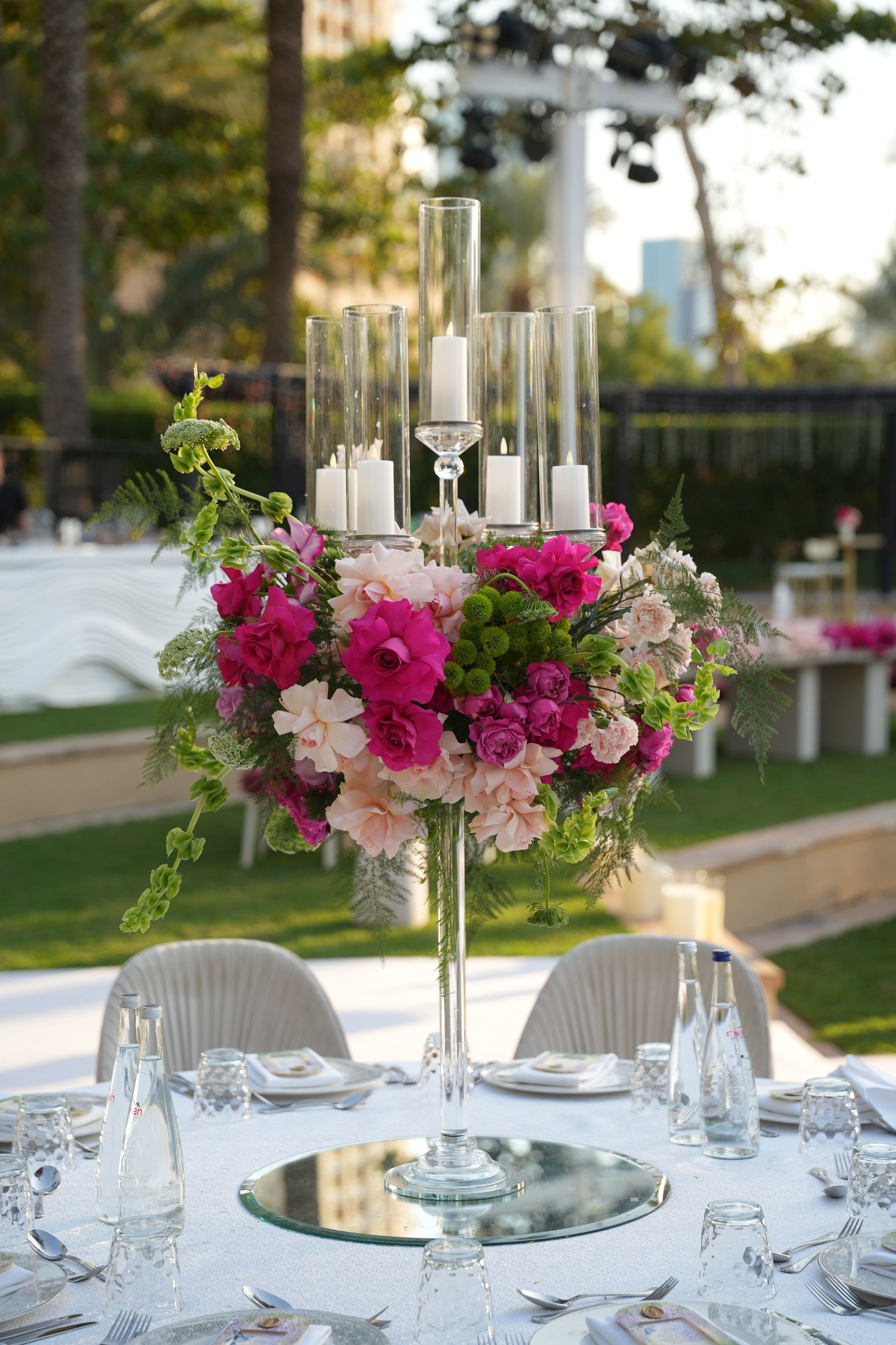 Tall glass candelabra crowned with fuchsia roses, peonies and trailing greenery on a mirrored base