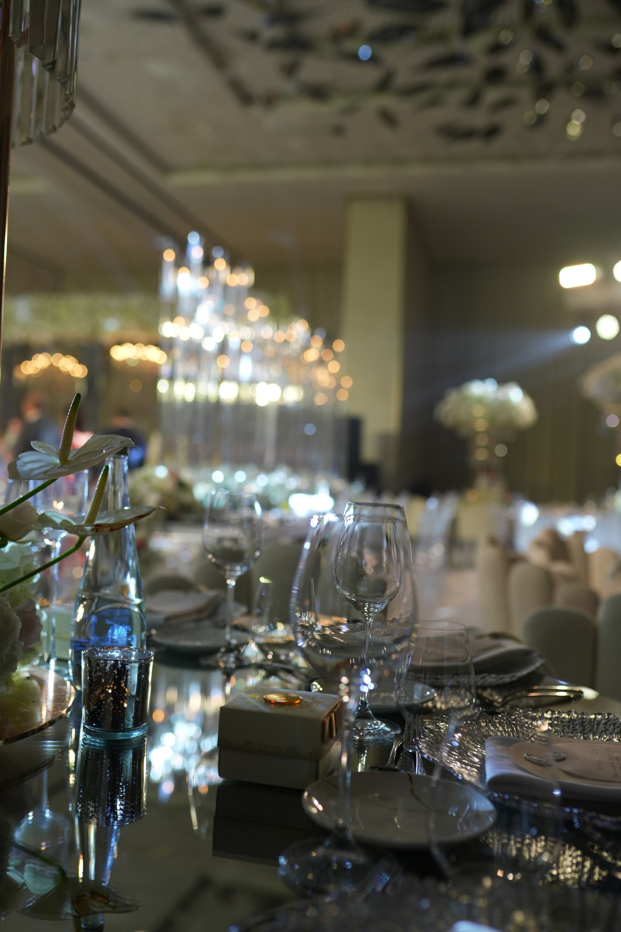 Glassware, favour box and white orchid on a mirrored table with candelabra glowing behind