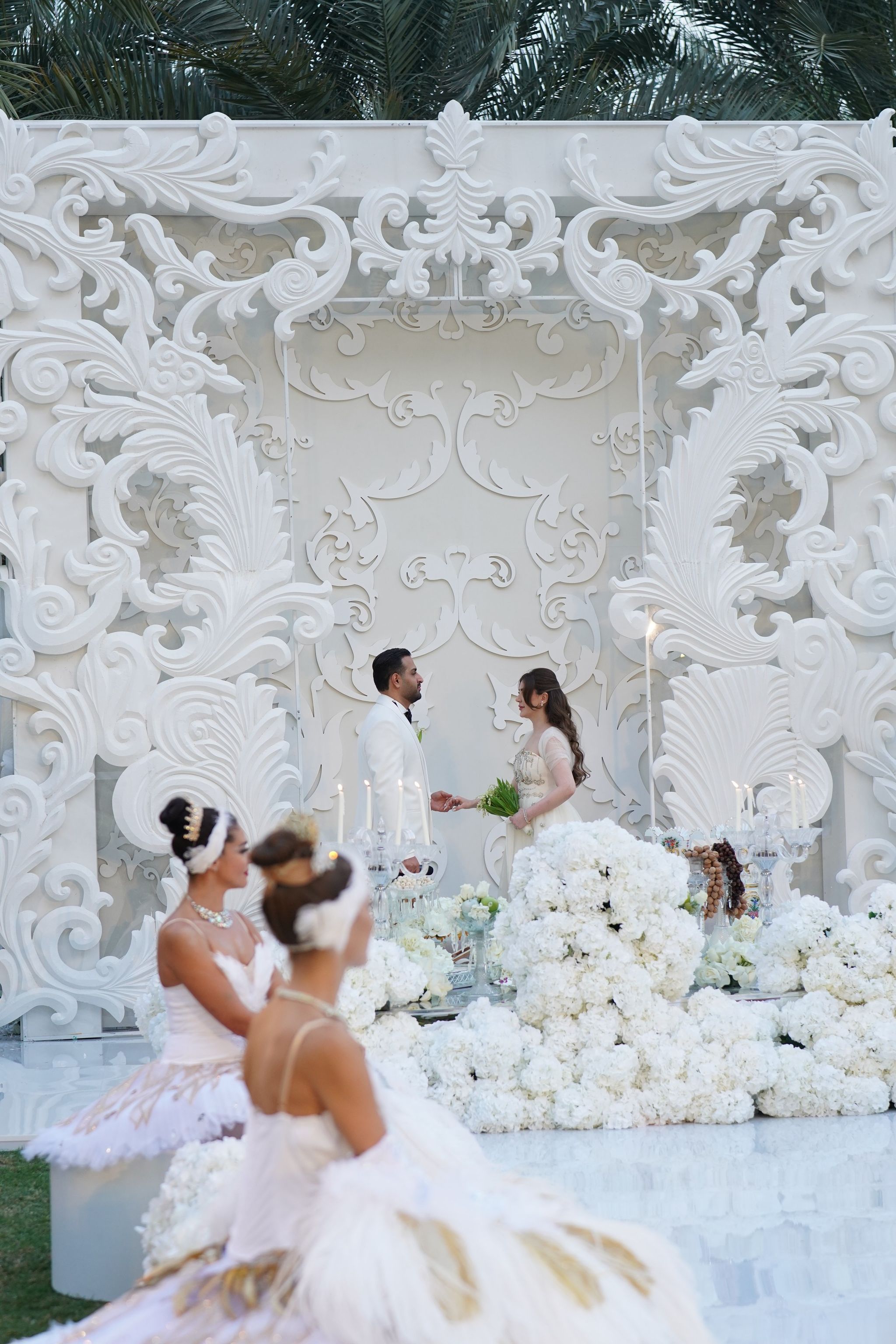 Ballerinas in white and gold tutus seated before a bank of white hydrangeas as the couple exchange vows