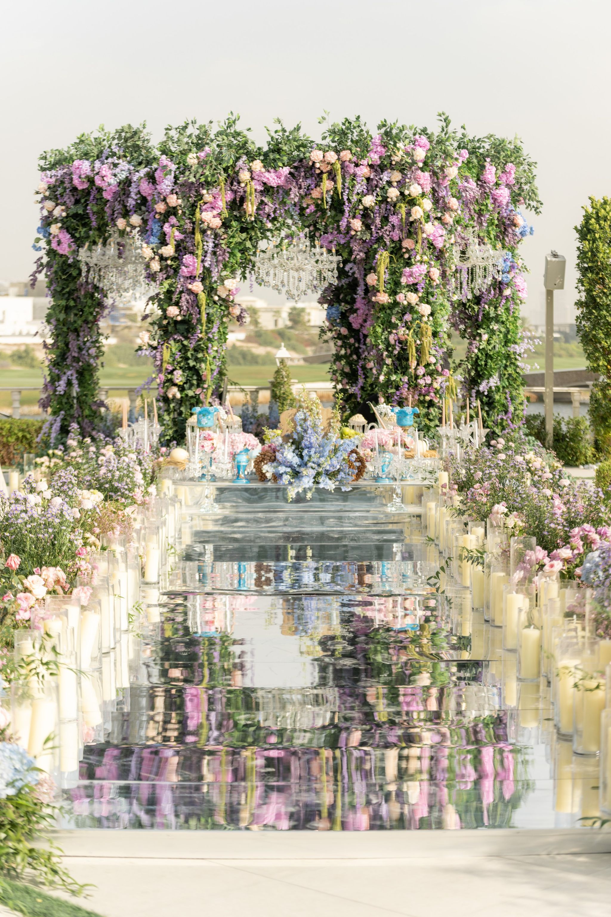 Candlelit mirrored aisle reflecting a canopy of wisteria, roses and crystal chandeliers