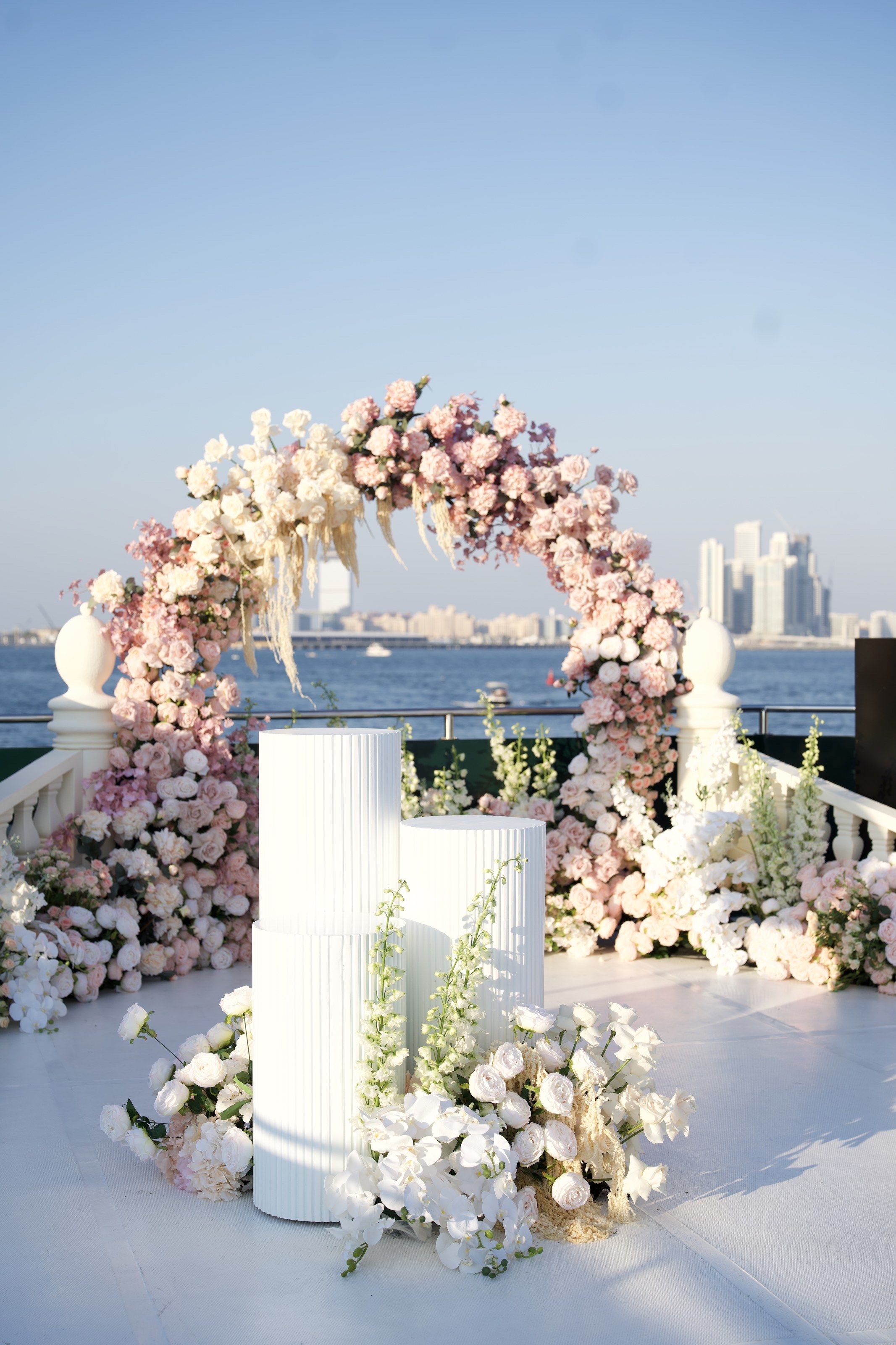 Blush and ivory rose arch with pampas grass and fluted white plinths on a yacht deck