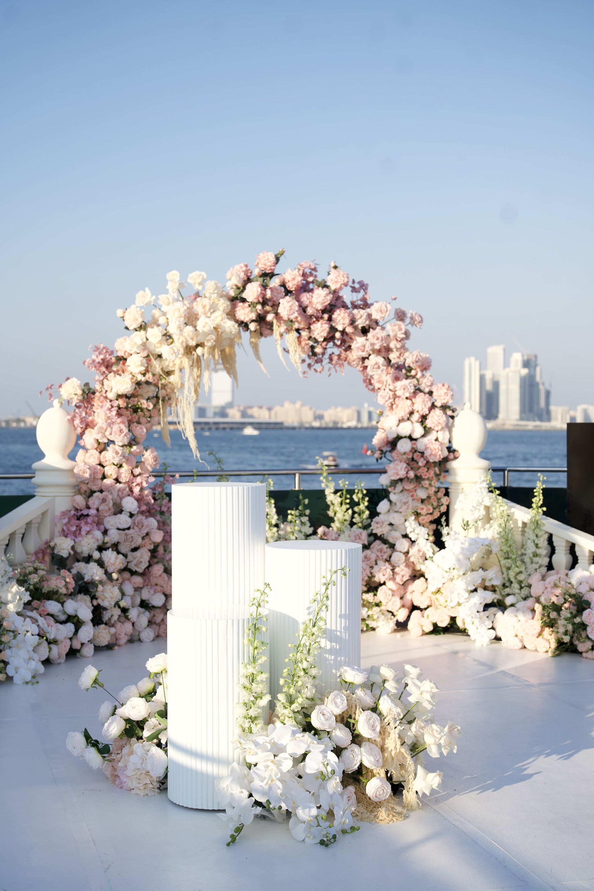 Blush and ivory rose arch with pampas grass and fluted white plinths on a yacht deck