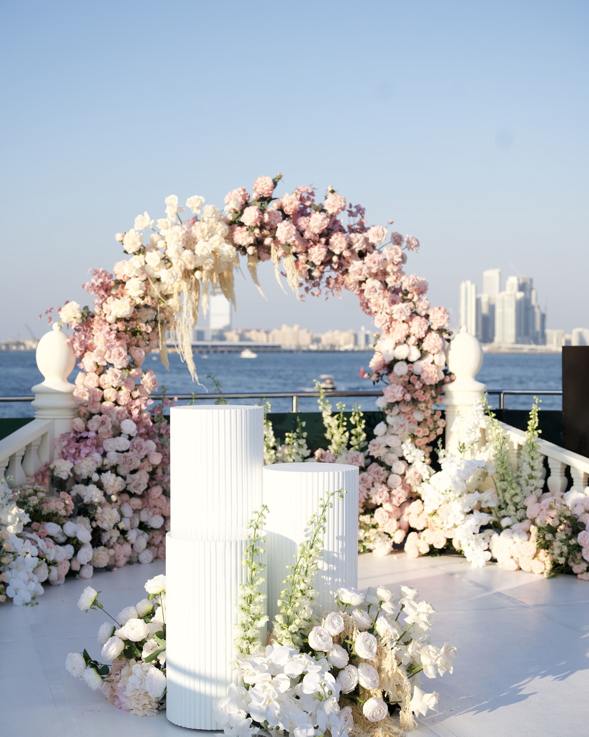 Blush and ivory rose arch with pampas grass and fluted white plinths on a yacht deck