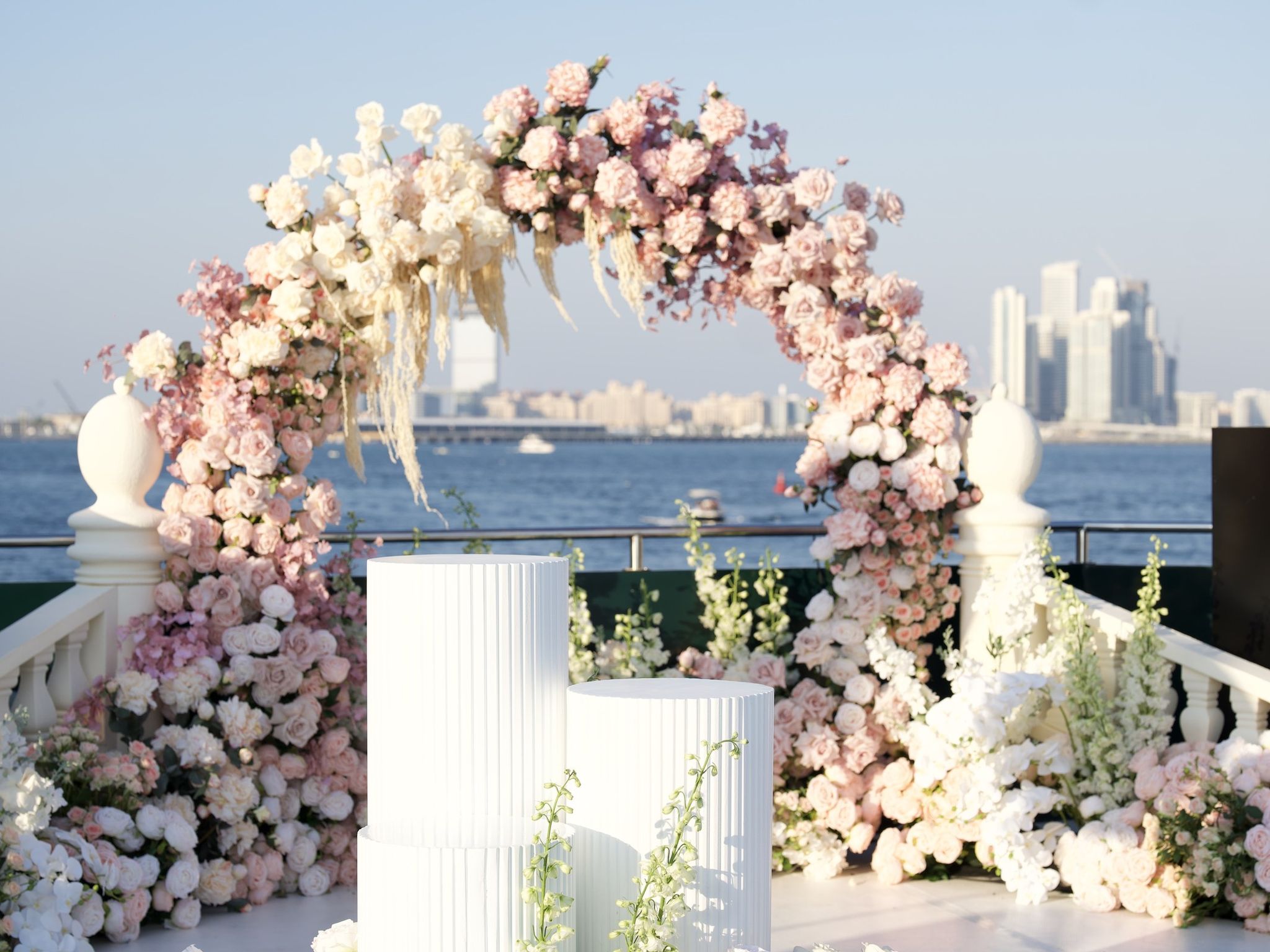 Blush and ivory rose arch with pampas grass and fluted white plinths on a yacht deck