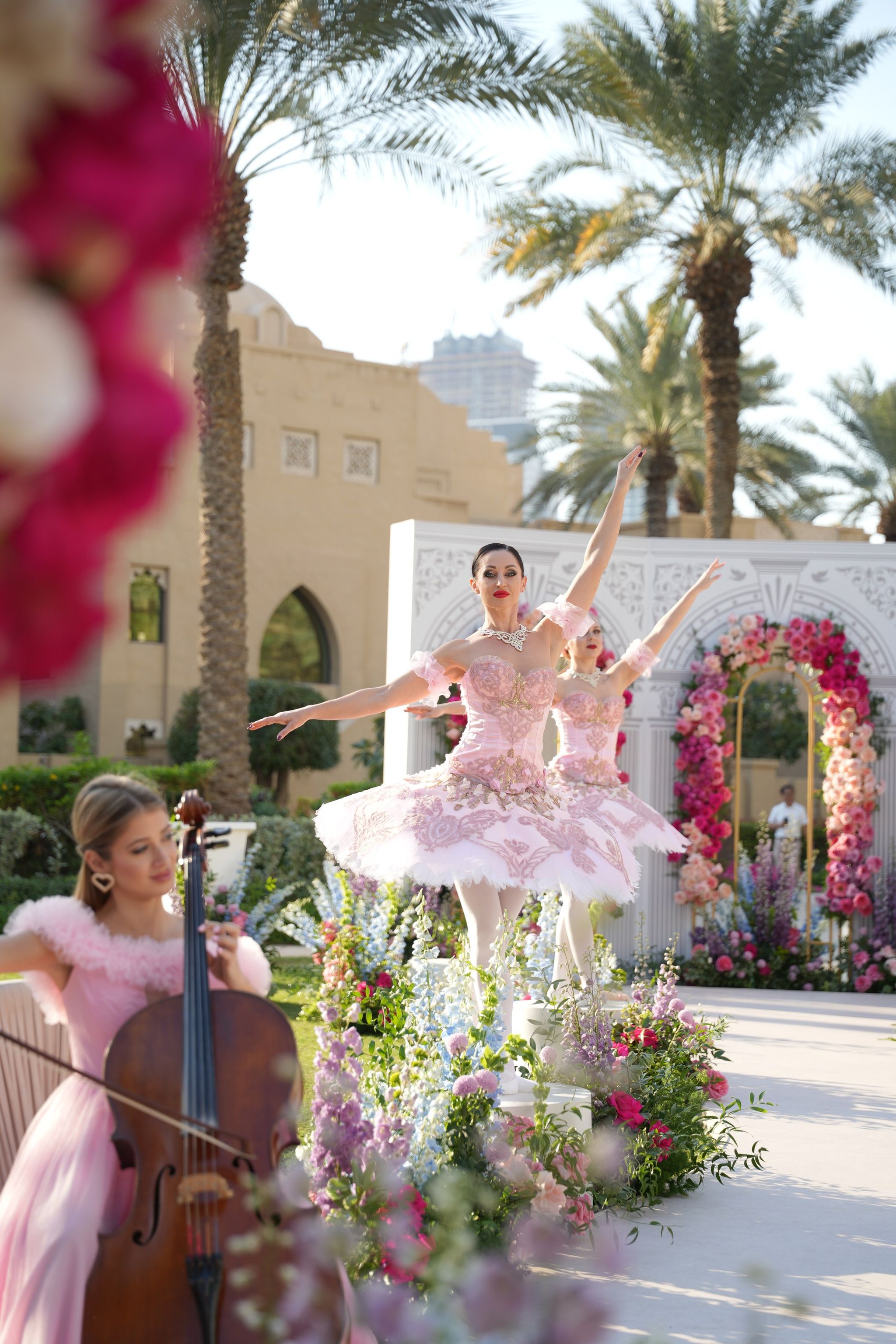 Ballerinas in embroidered blush tutus dancing on the aisle as a cellist plays