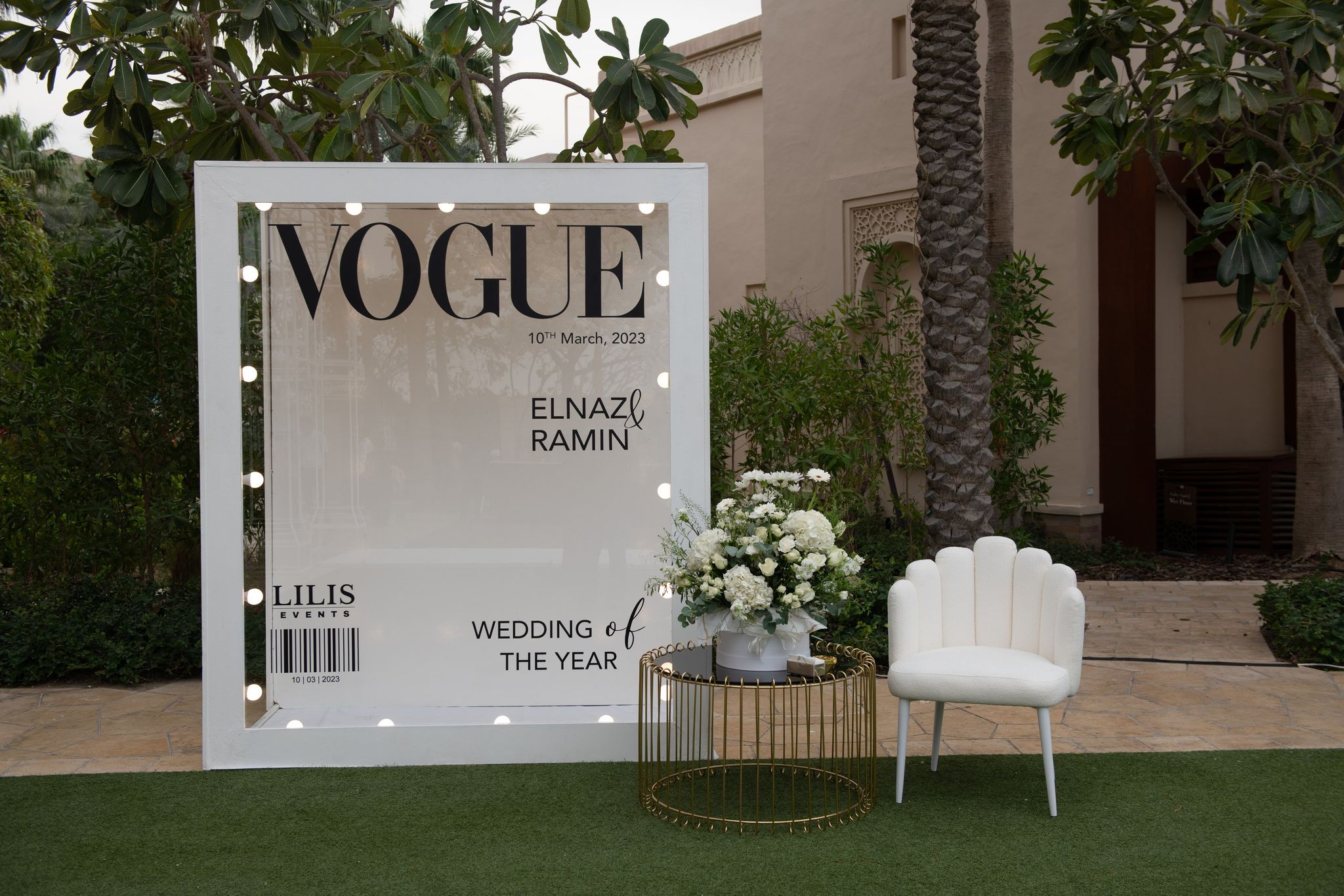 Illuminated magazine-cover photo board beside a scalloped white chair and gold side table