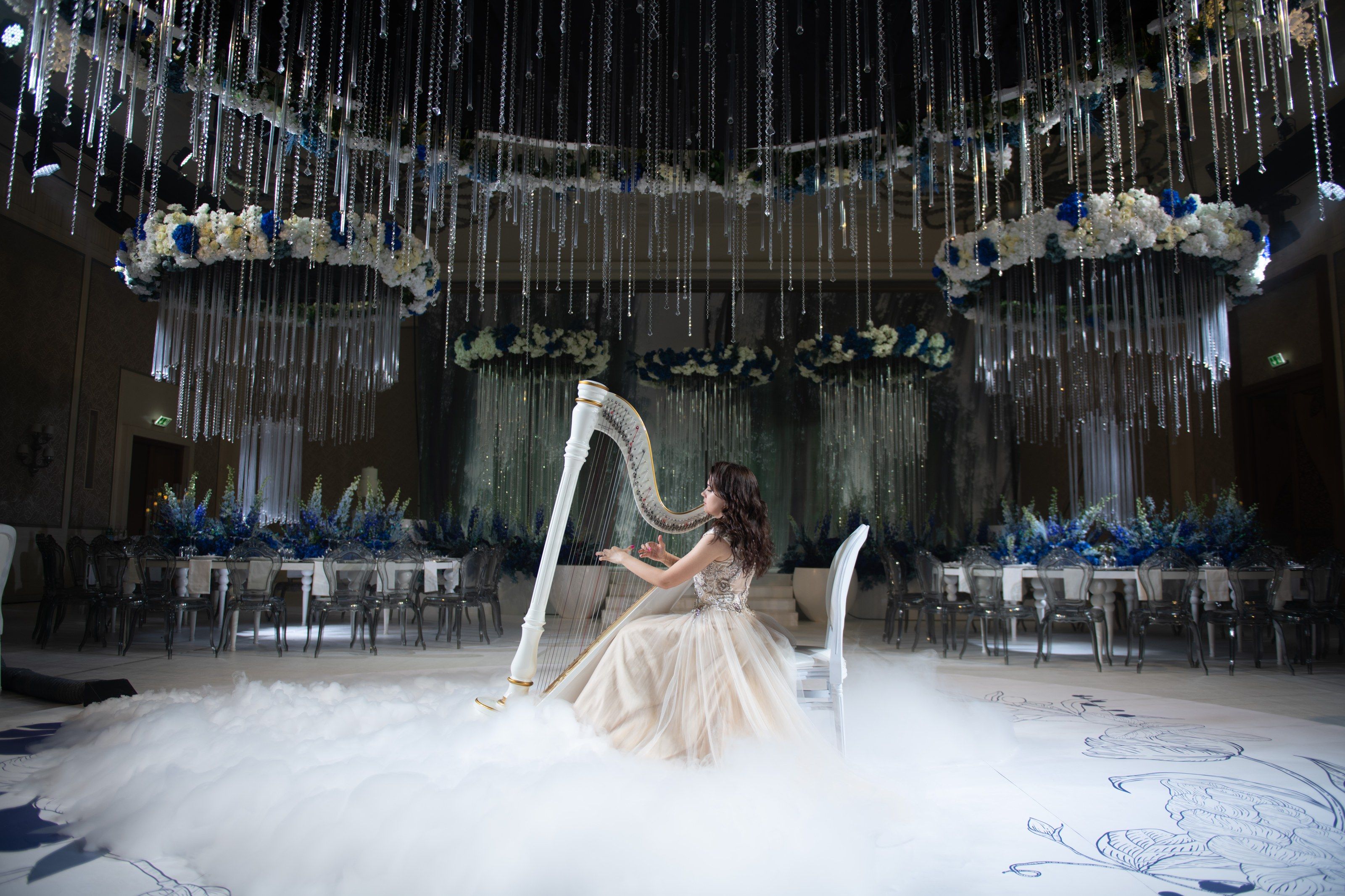 A harpist seated in low fog beneath crystal-hung floral rings at Four Seasons Resort Dubai at Jumeirah Beach