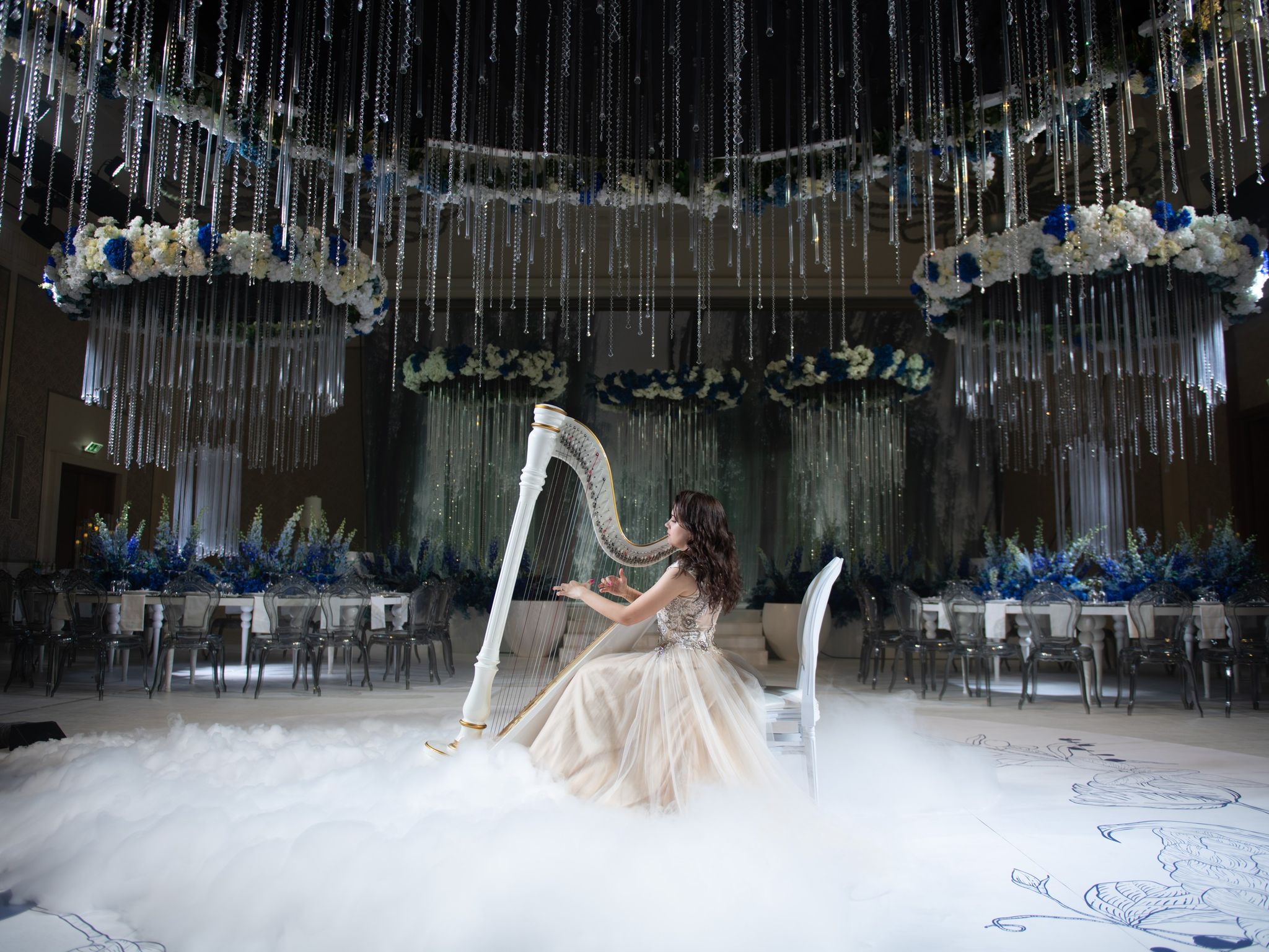 A harpist seated in low fog beneath crystal-hung floral rings at Four Seasons Resort Dubai at Jumeirah Beach
