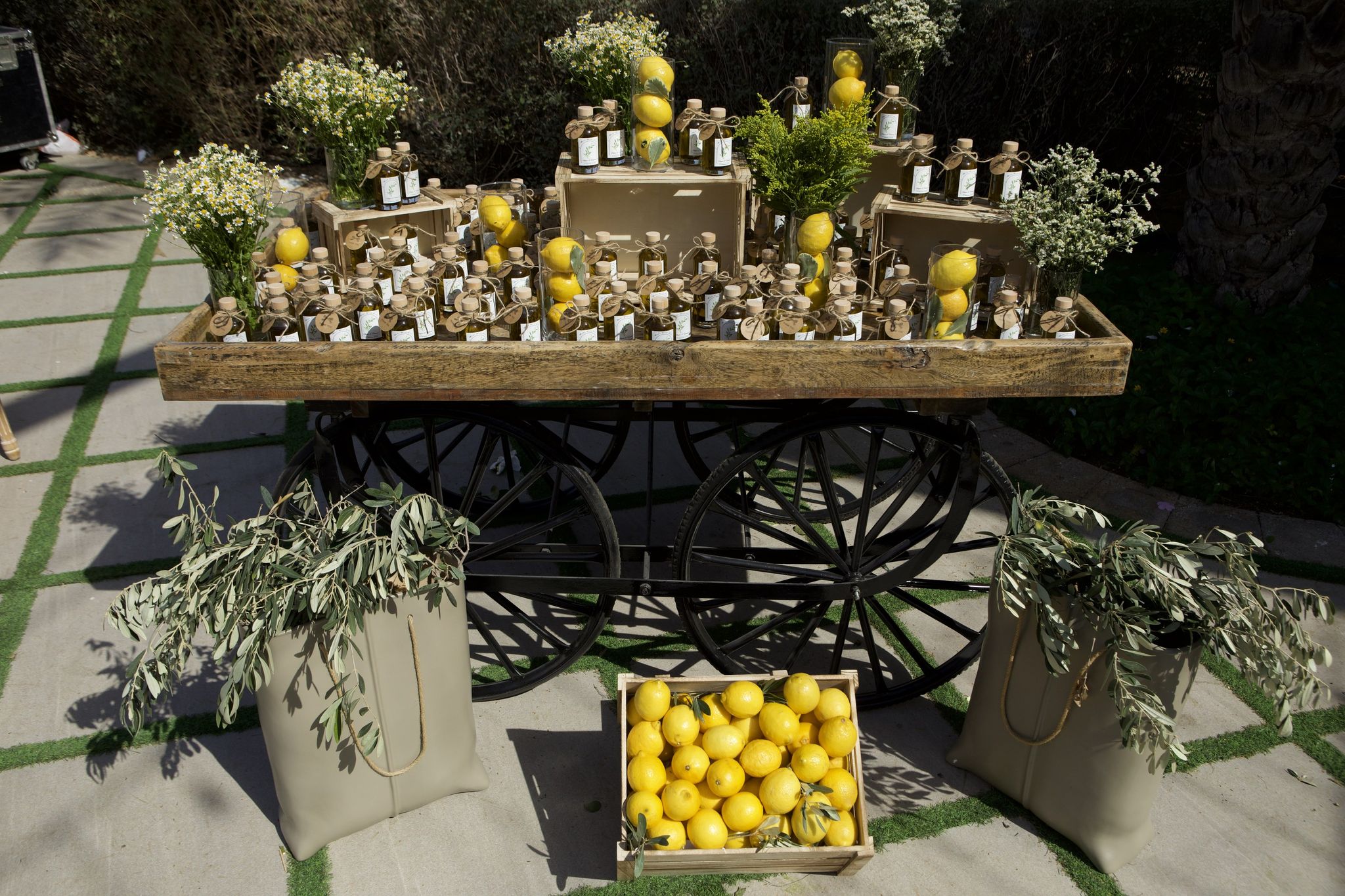 Olive-oil favours and jars of lemons on a wooden cart in strong afternoon shadow