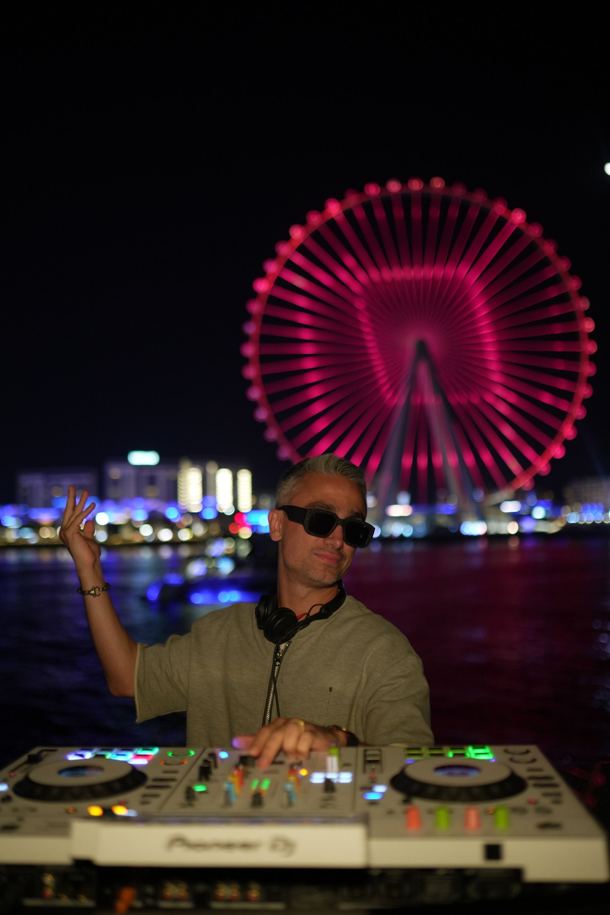 DJ at the decks on a private yacht at night, with Ain Dubai lit pink behind