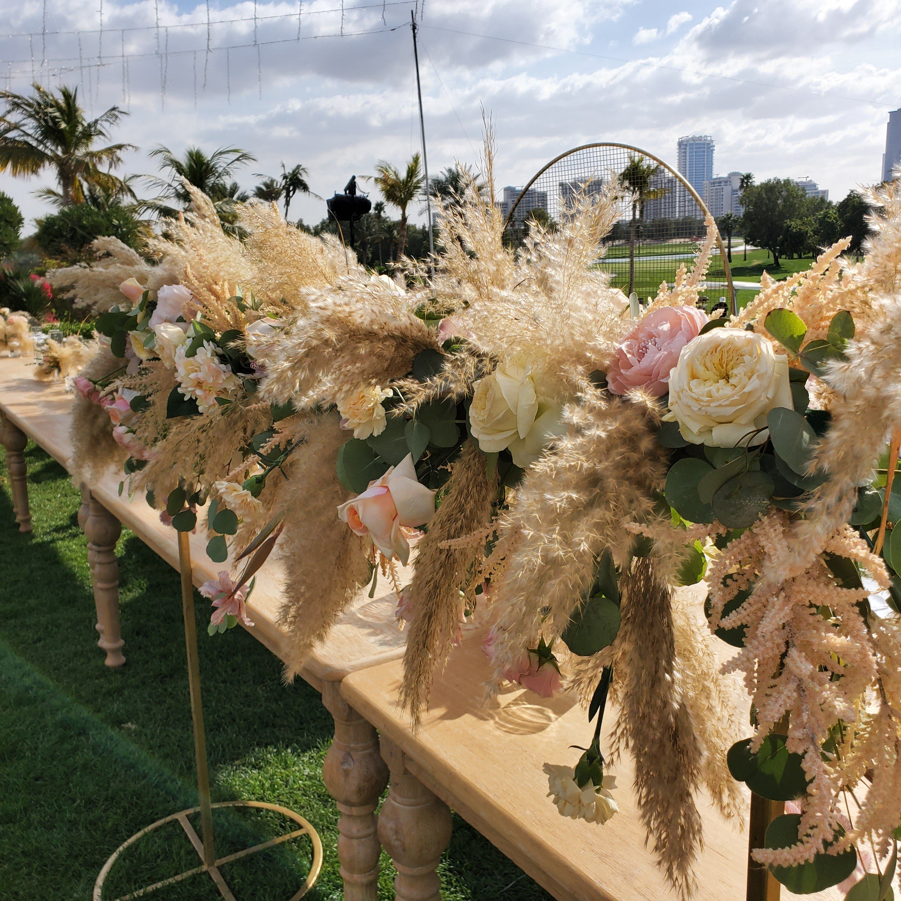 Long wooden table garlanded with pampas grass, garden roses and astilbe on the lawn at Emirates Golf Club