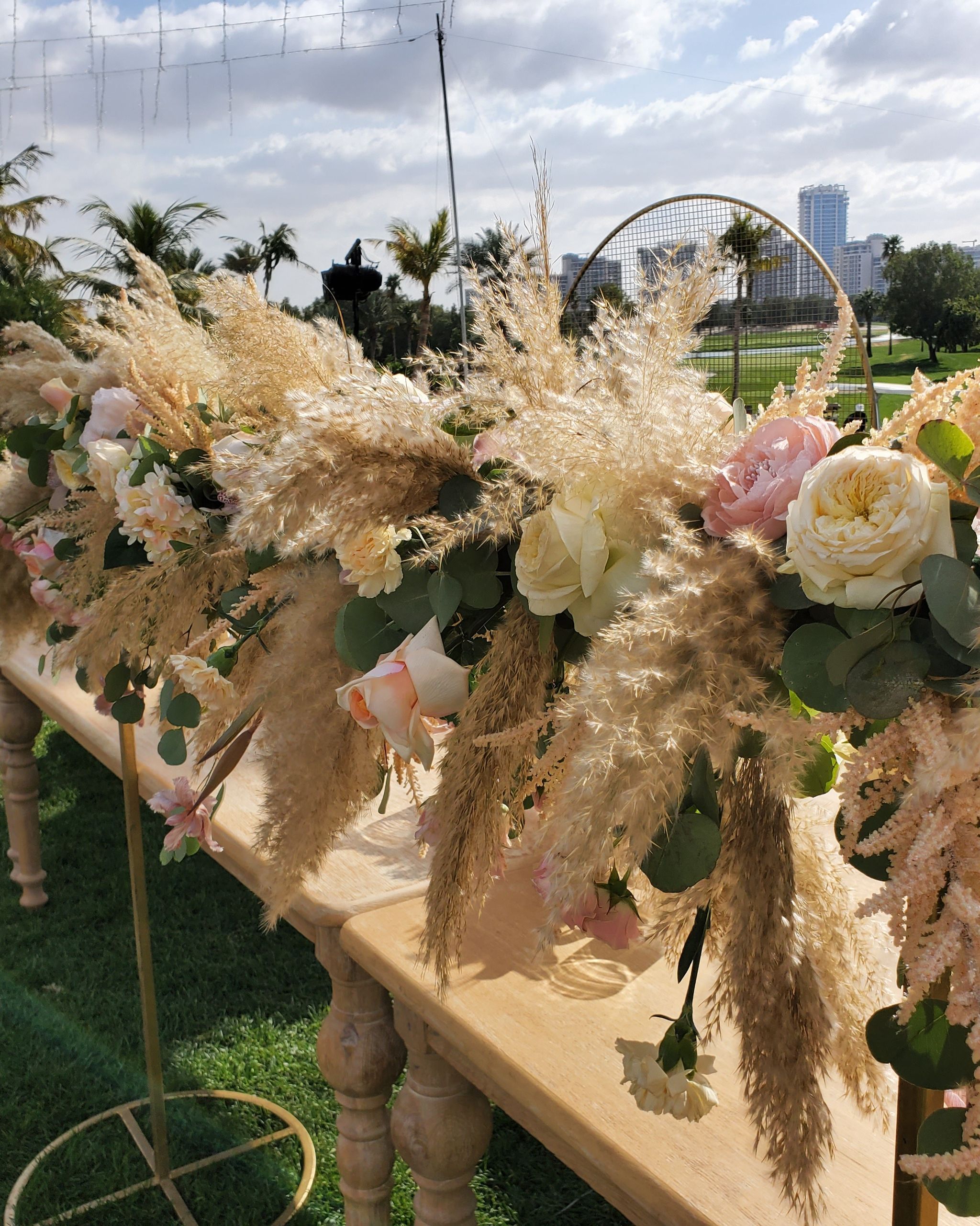 Long wooden table garlanded with pampas grass, garden roses and astilbe on the lawn at Emirates Golf Club